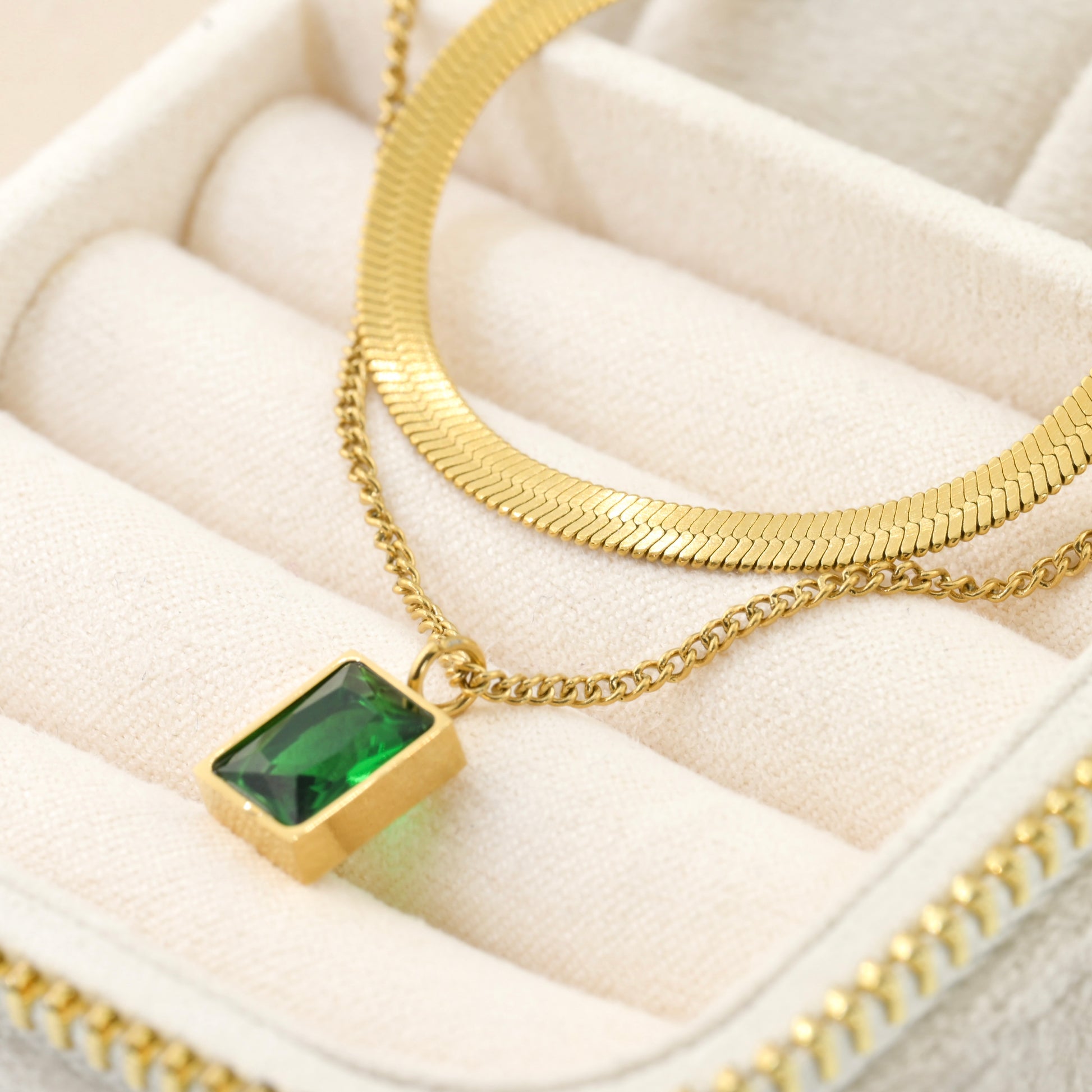 Gold necklace with a green gemstone pendant on a white cushioned surface