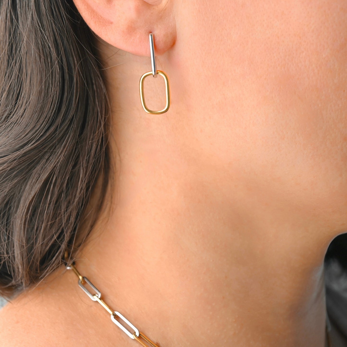 Gold linked rectangular hoop earring worn by a person with a neutral background