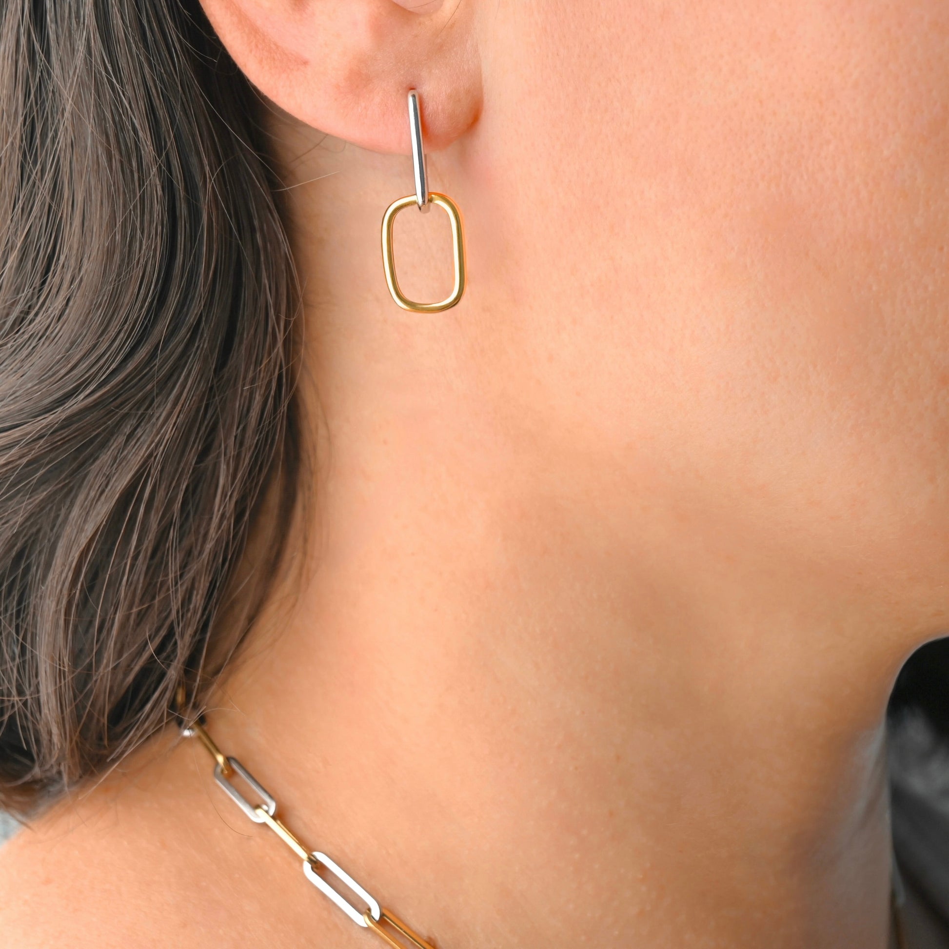 Gold linked rectangular hoop earring worn by a person with a neutral background