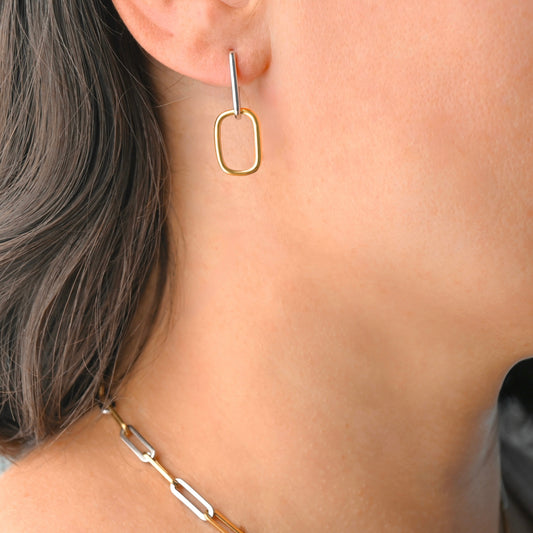 Gold linked rectangular hoop earring worn by a person with a neutral background