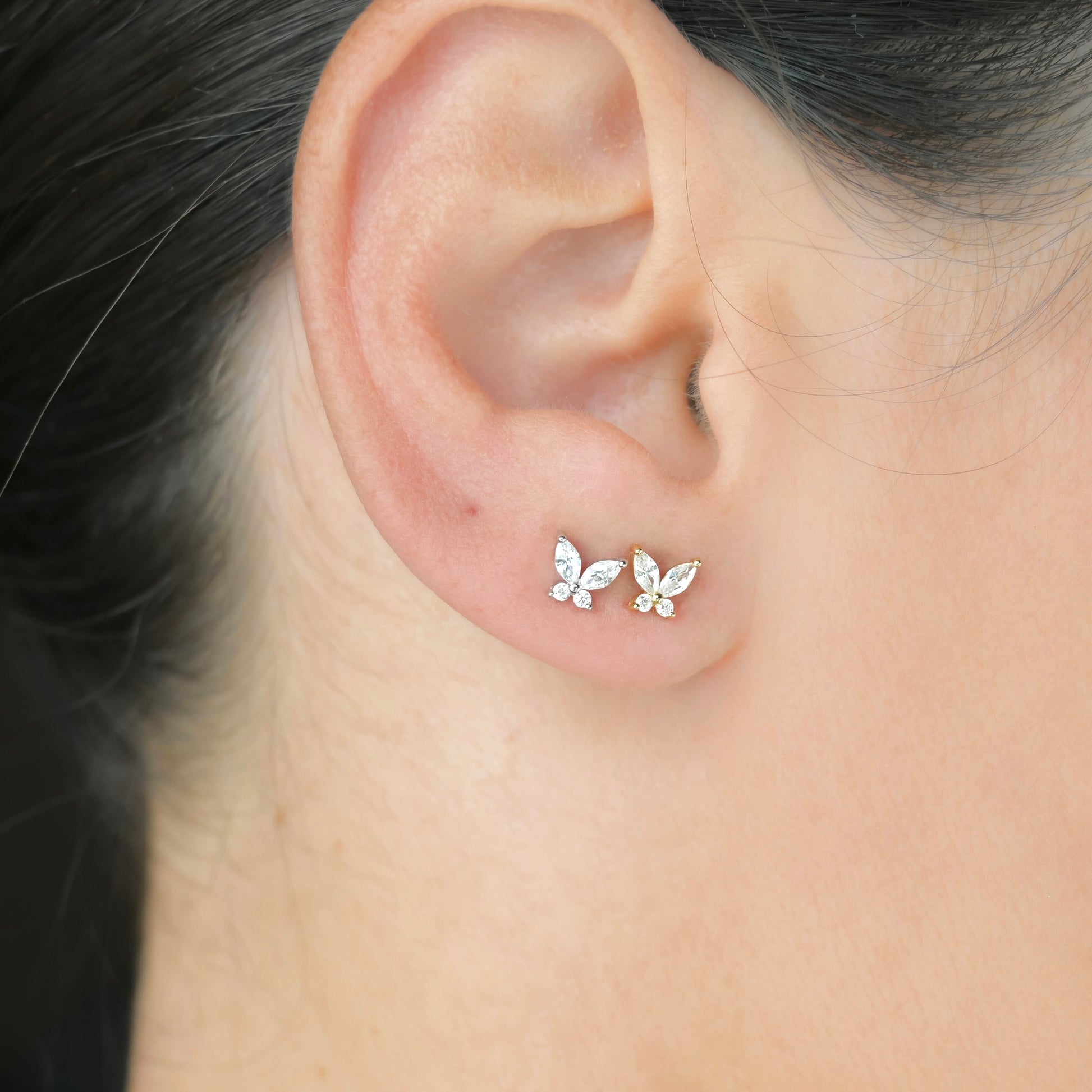 Diamond butterfly stud earrings, one gold and one silver, worn on an ear