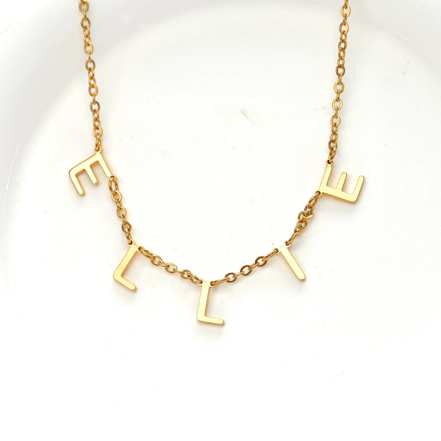 A gold initial necklace spelling 'ELLIE' on a delicate chain, displayed on a clean white background.