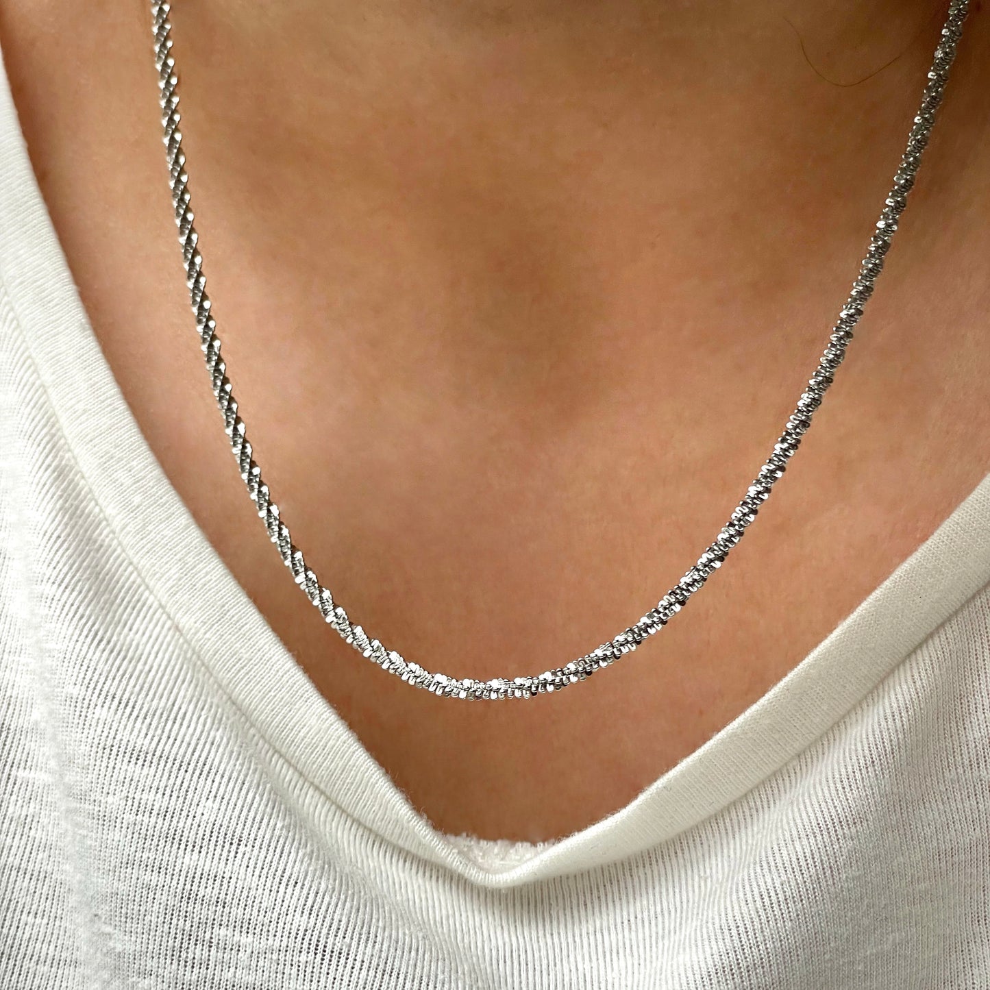 Silver shimmer chain necklace worn by a person with a white shirt