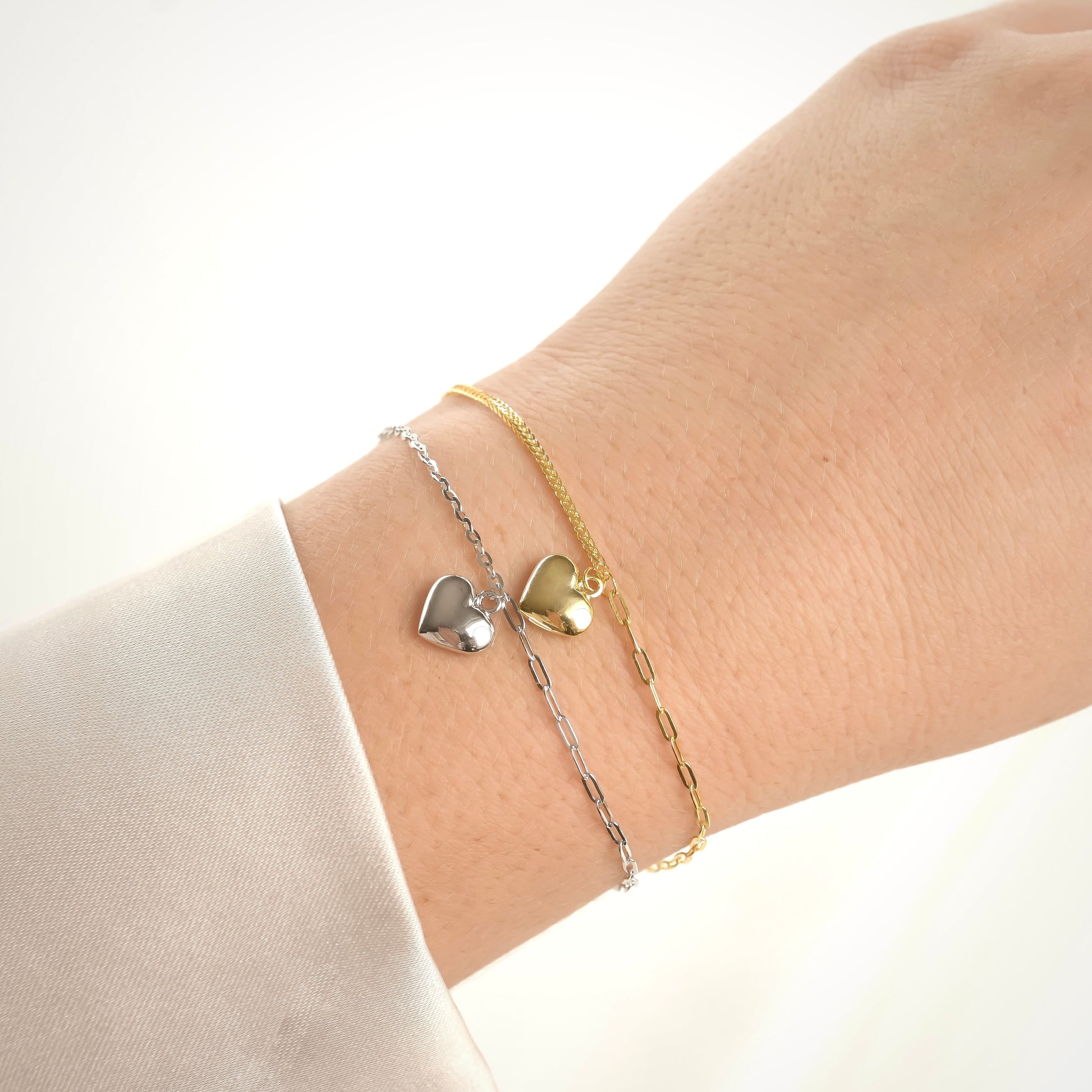 Two heart charm bracelets  with mixed chains on a wrist against a white background