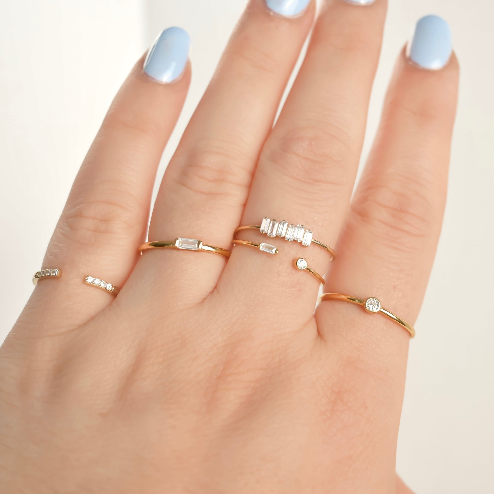 Hand wearing multiple gold rings with small gemstones on a light background