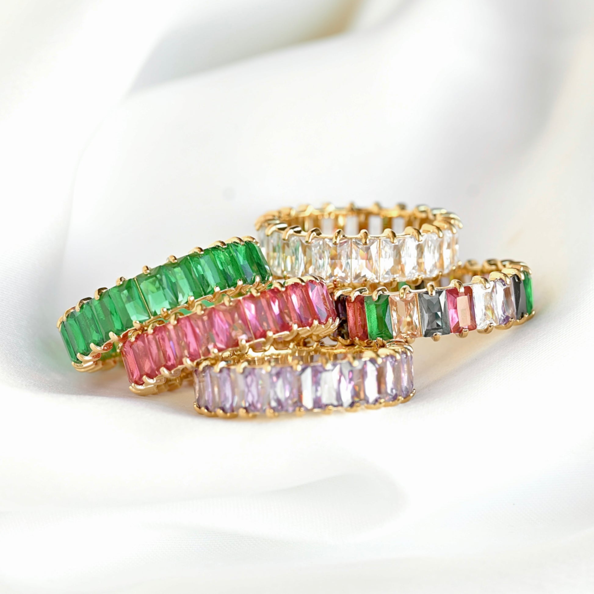 Five gold rings with green, pink, purple, white and mixed color gemstones on a white background