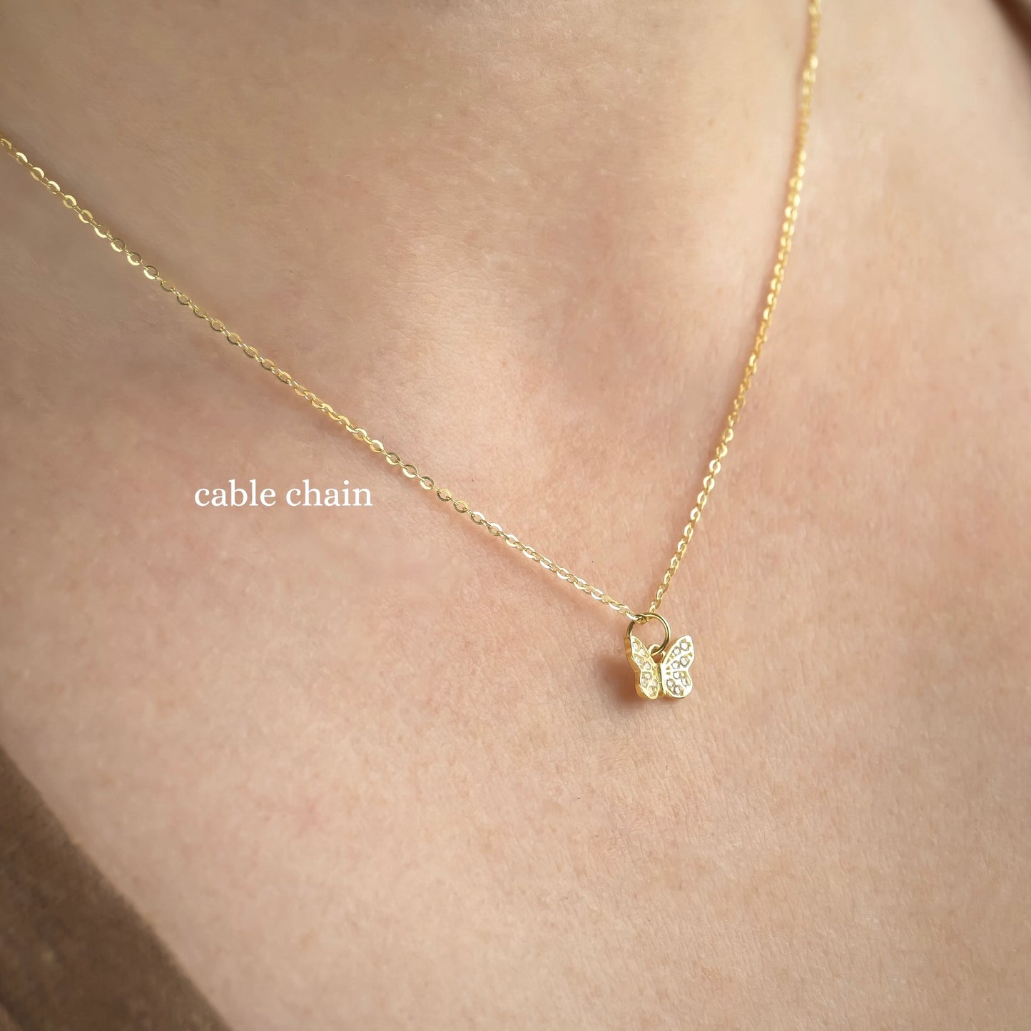 Gold butterfly necklace on a person's neck with 'cable chain' label