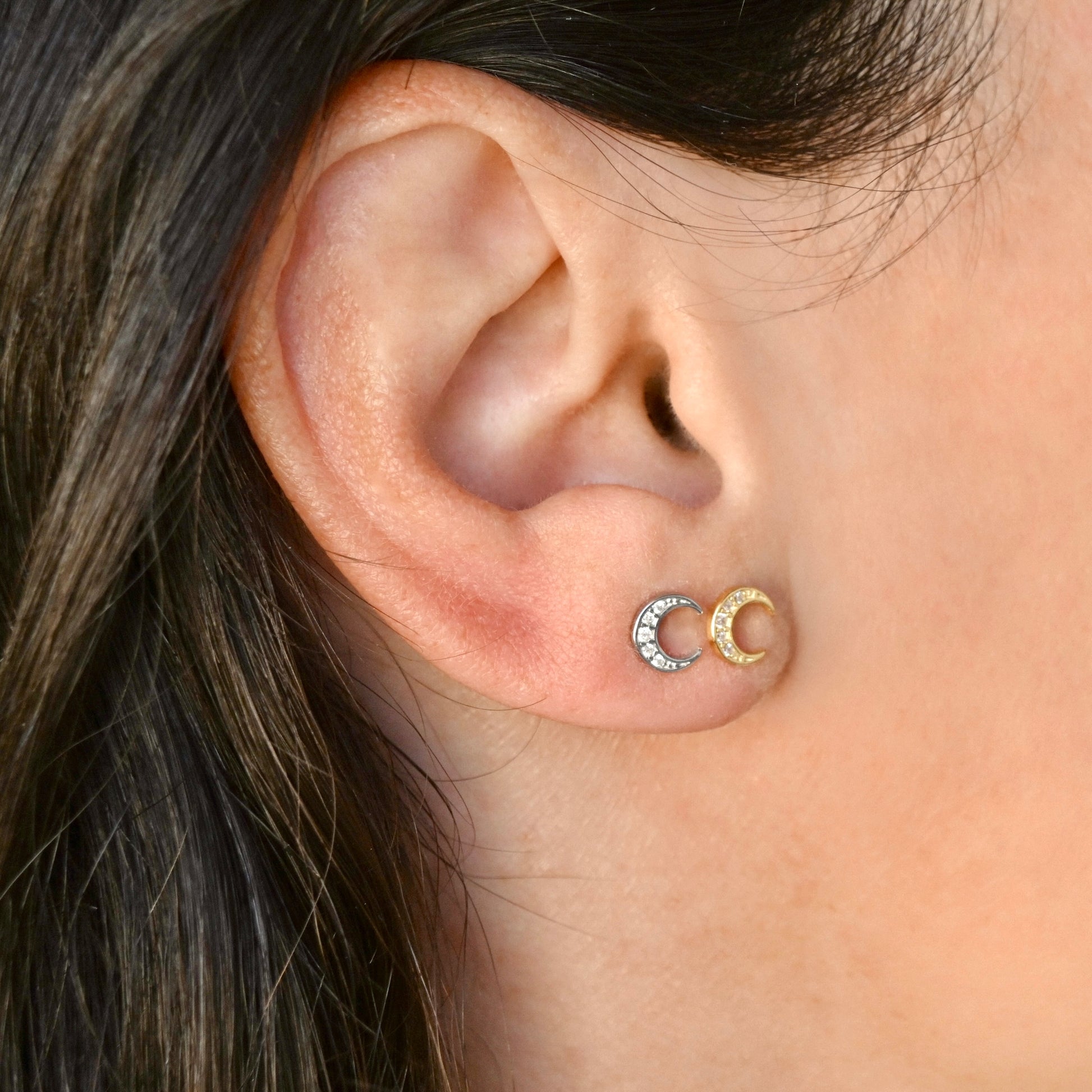 Close-up of an ear wearing gold and silver crescent studs.