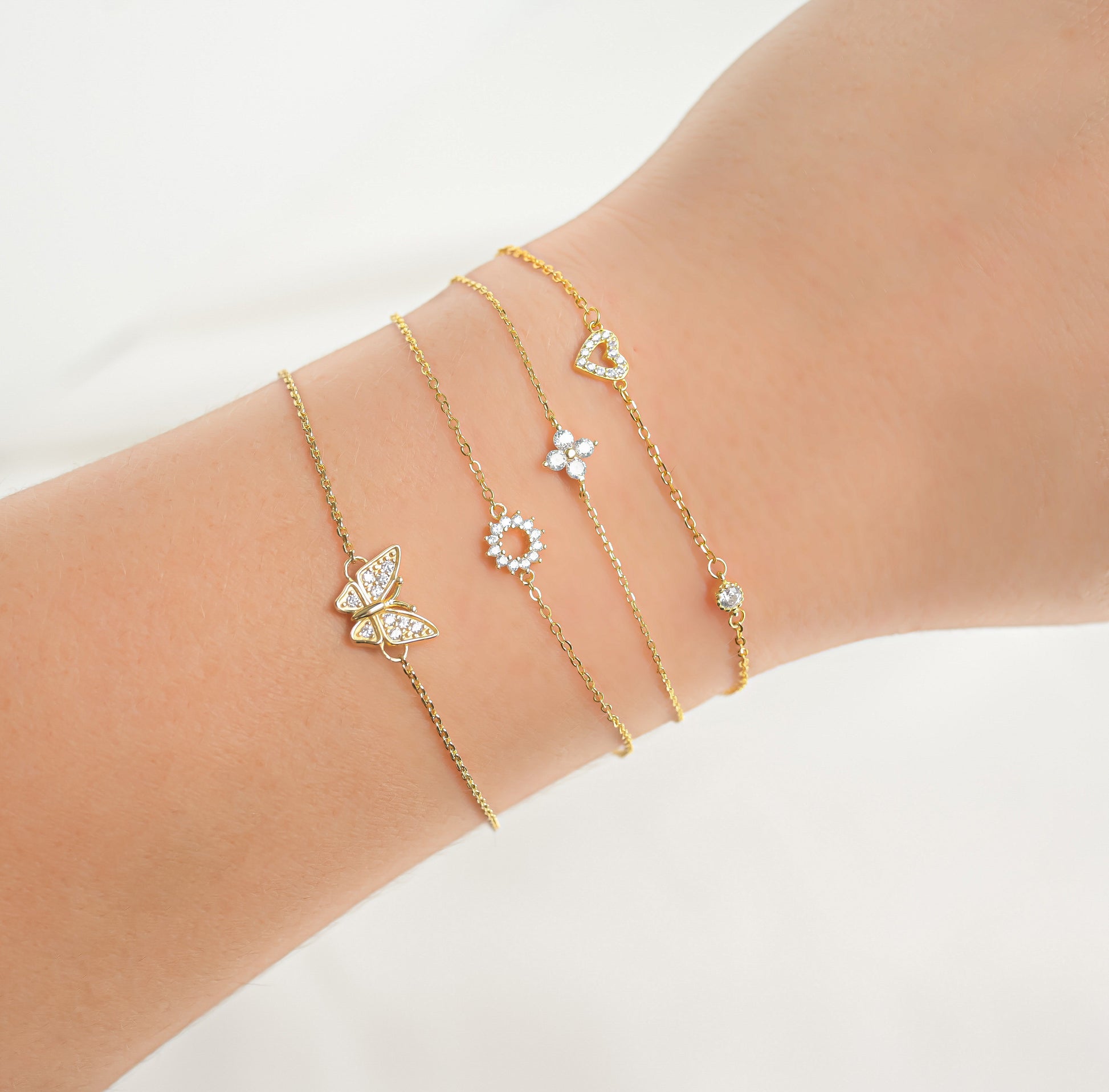 Gold bracelet with butterfly, sun and clover and heart charms on a wrist against a white background