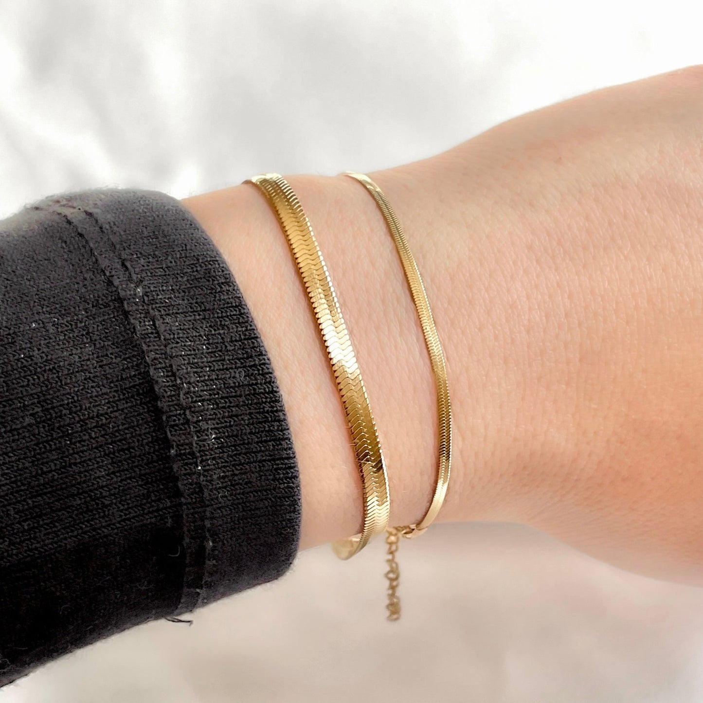 Gold flate snake bracelets of two different widths on a wrist with a blurred background