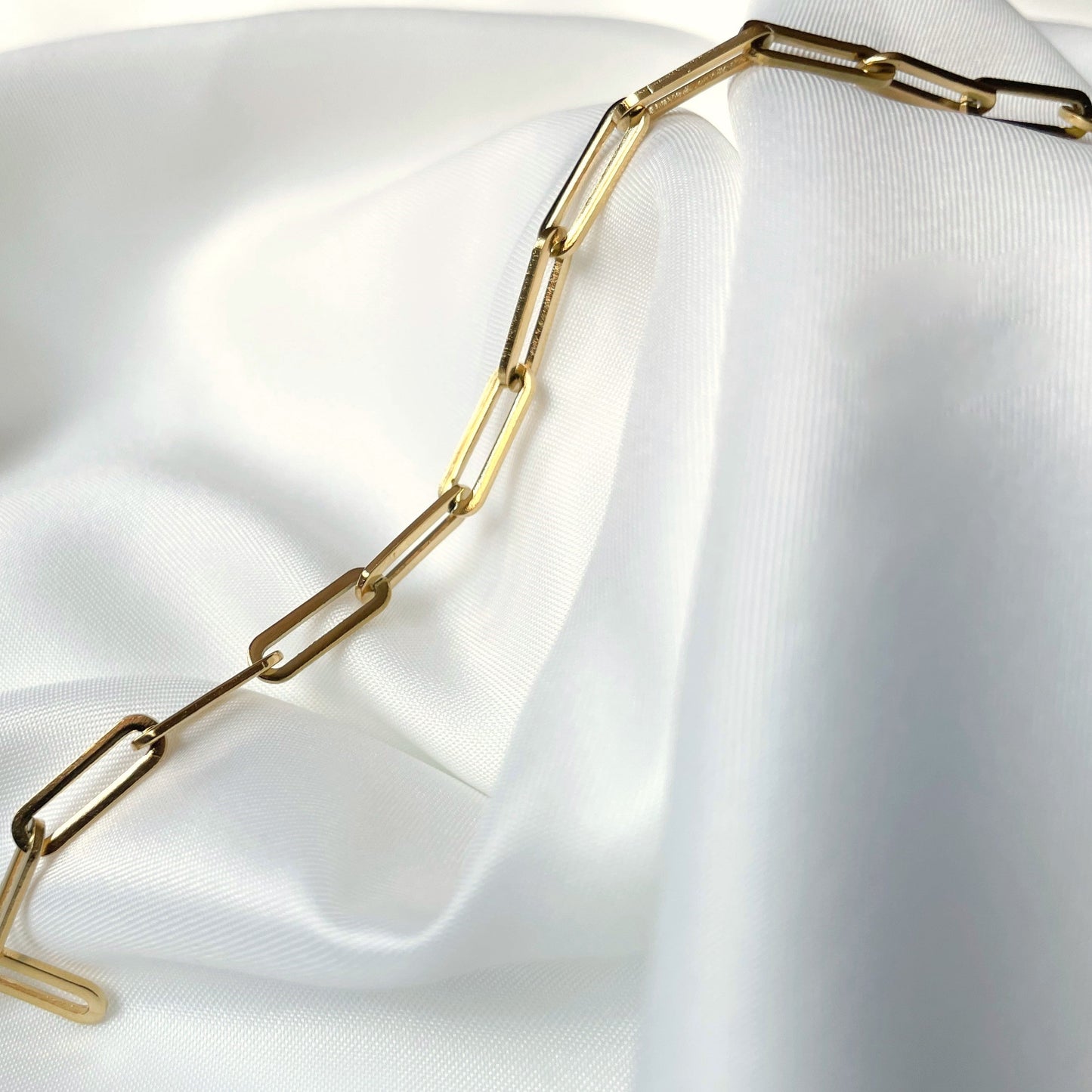 Gold paperclip chain necklace on a white fabric background