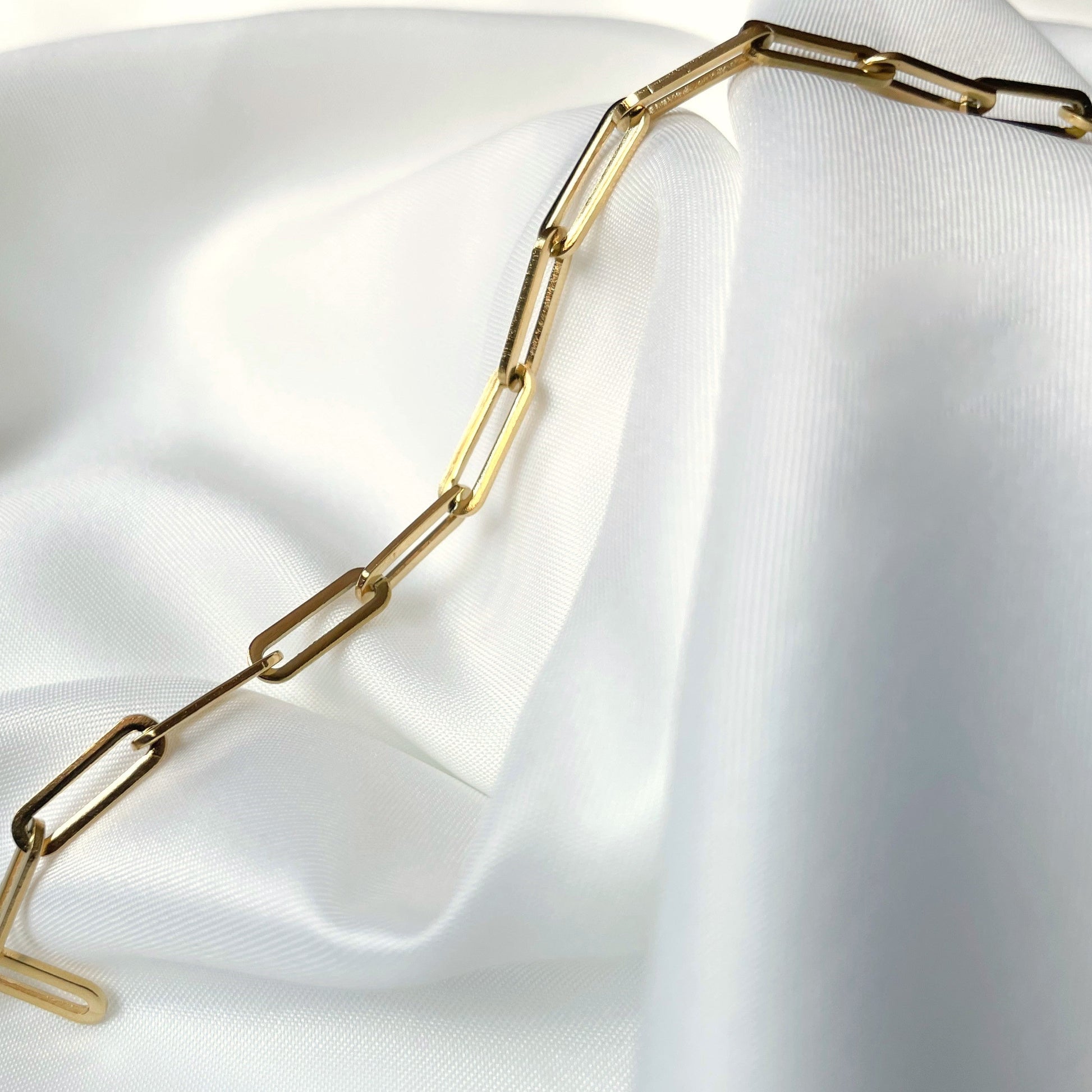 Gold paperclip chain necklace on a white fabric background