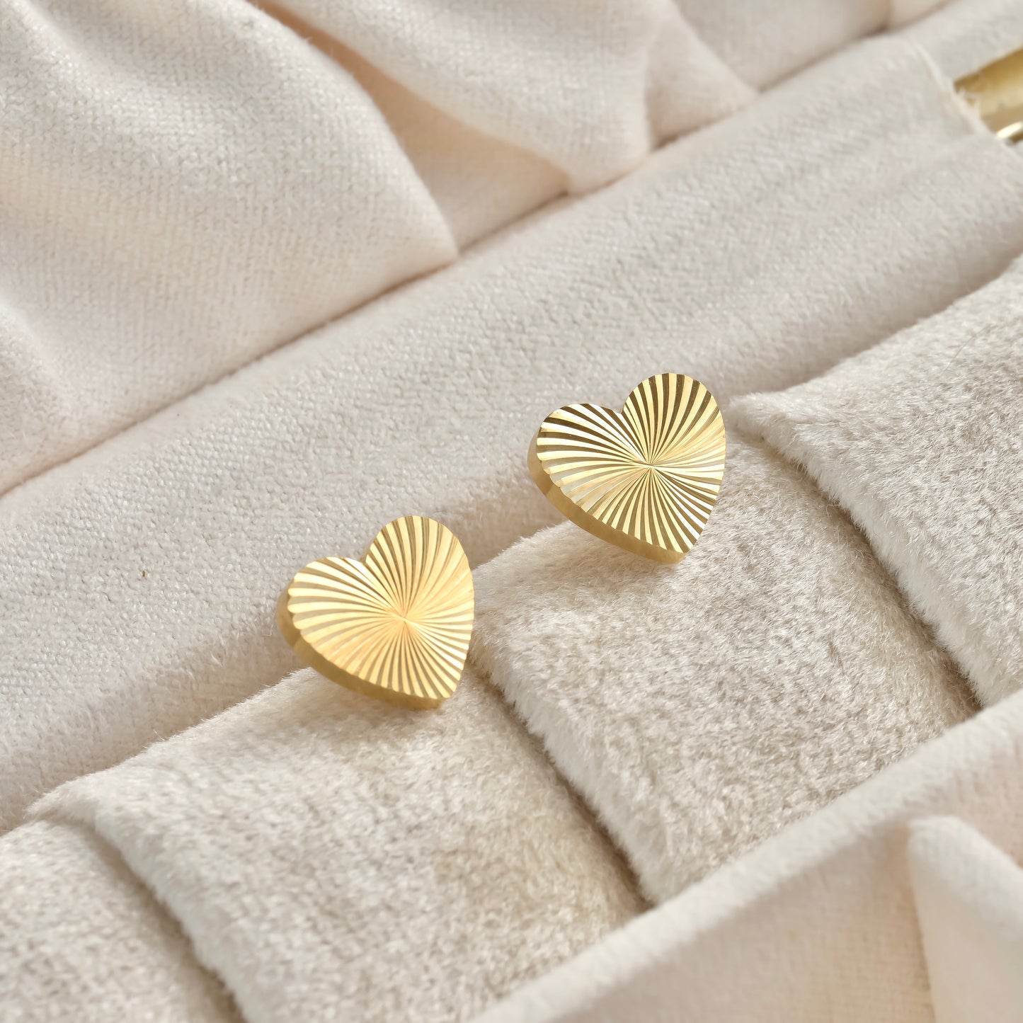 Gold textured heart earrings on a textured beige surface