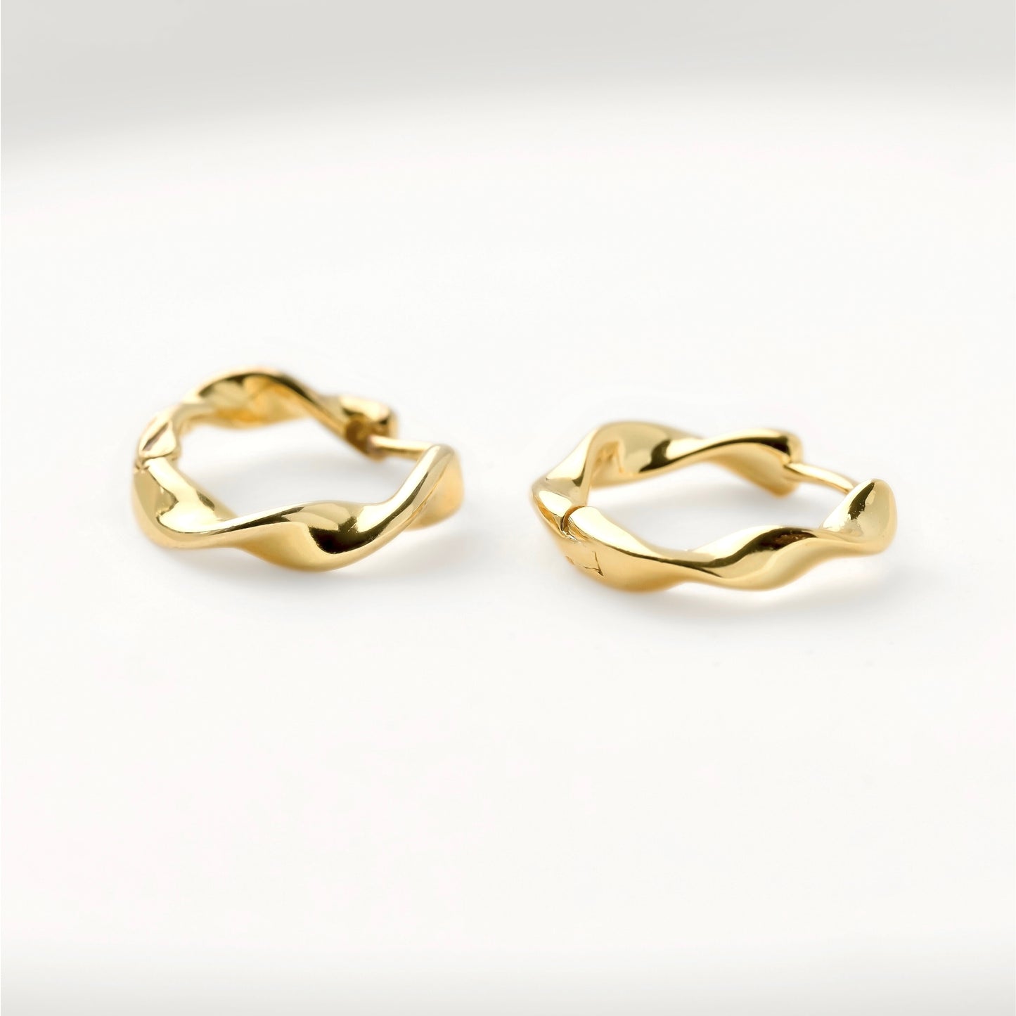 Twisted gold hoop earrings on a light gray background