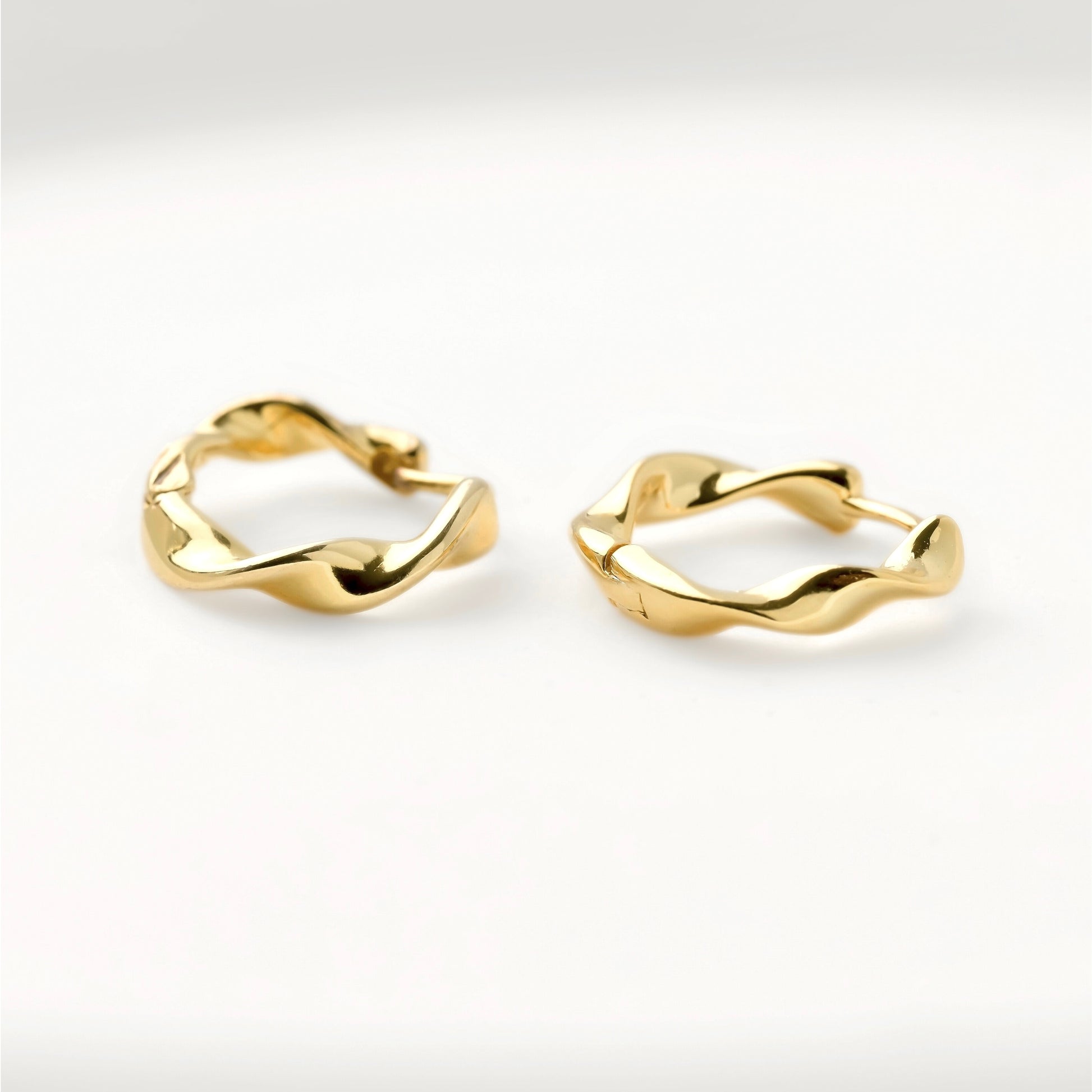 Twisted gold hoop earrings on a light gray background