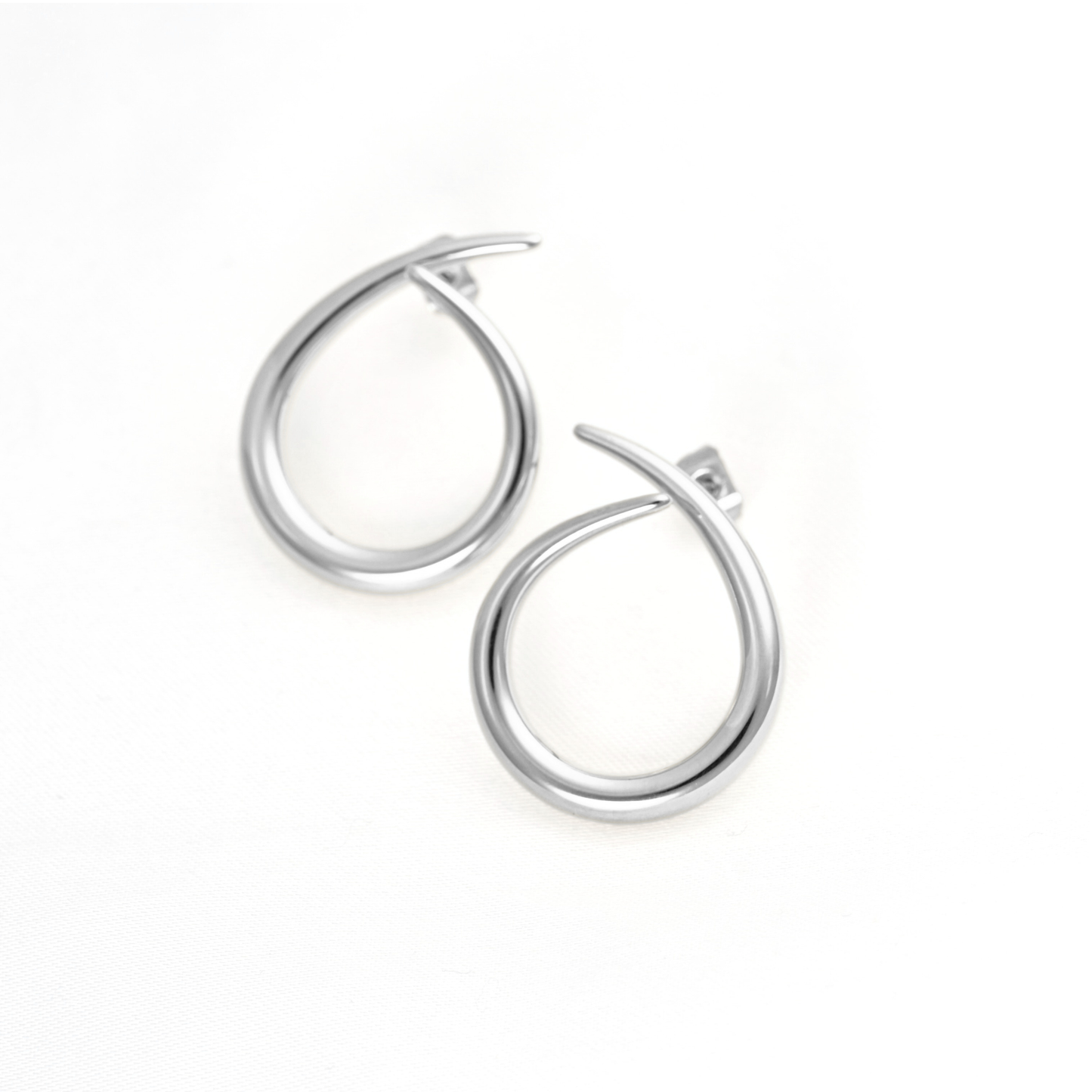 A pair of polished silver hoop earrings with a unique open, teardrop-like design, displayed on a clean white background.