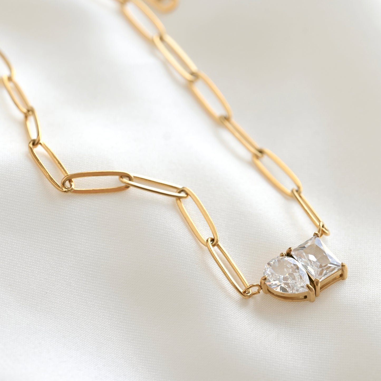 Gold elongated paperclip chain necklace with a pear and rectangular stones on a light background