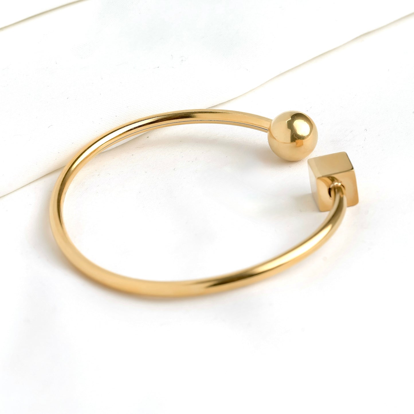 Close-up view of gold cue and ball  cuff bracelet with spherical and square ends on a white background