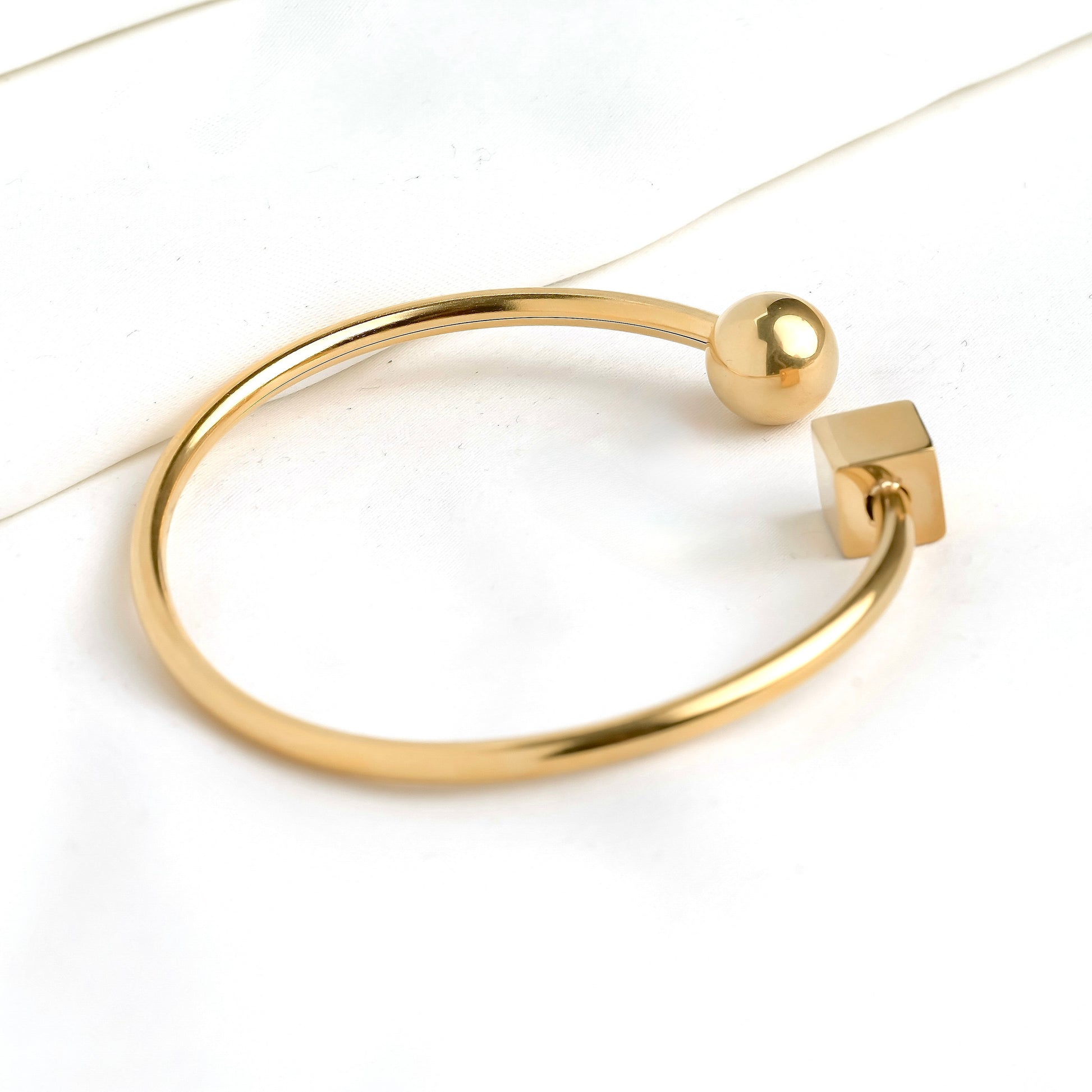 Close-up view of gold cue and ball  cuff bracelet with spherical and square ends on a white background