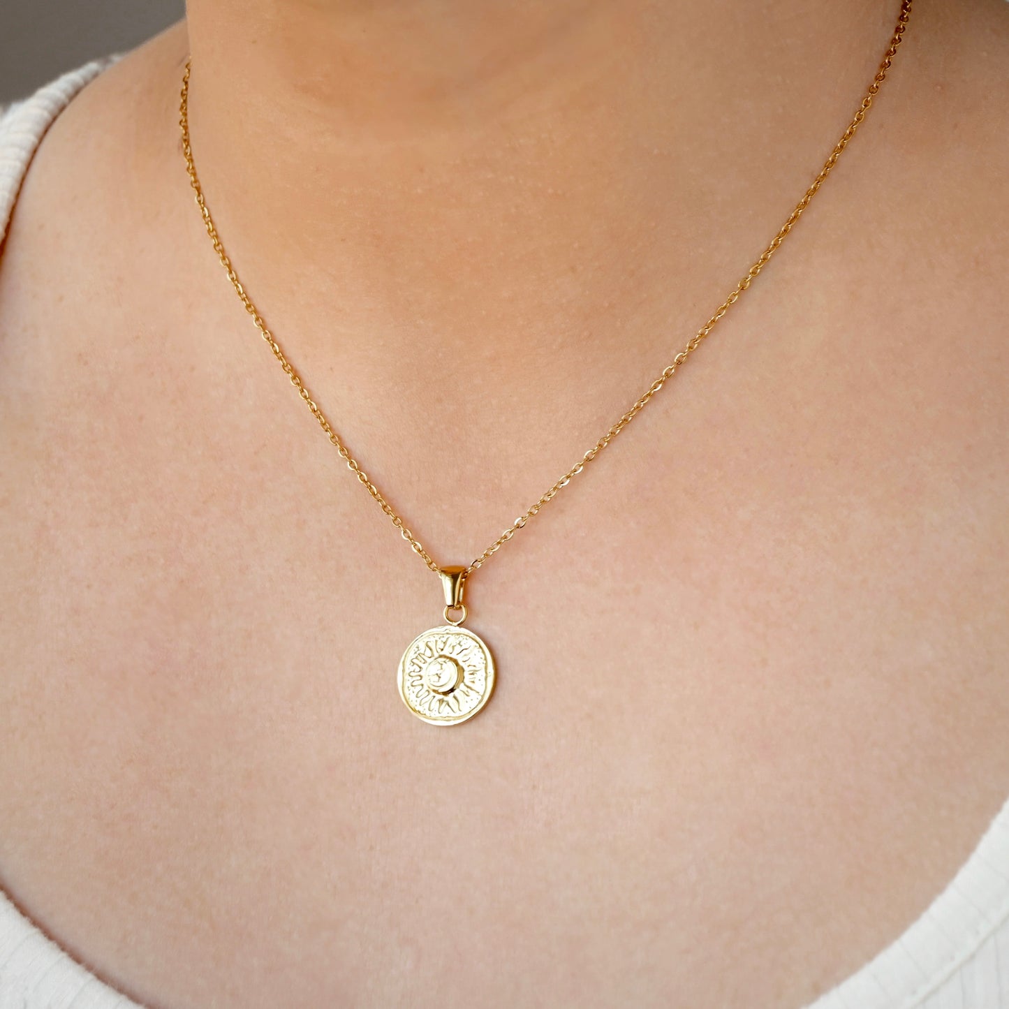 Gold vintage style necklace with a round pendant on a person wearing a white top.