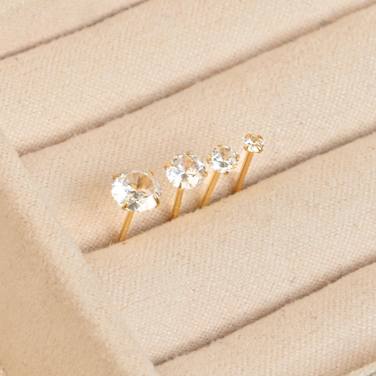 Set of gold stud earrings with clear gemstones in a beige ring tray