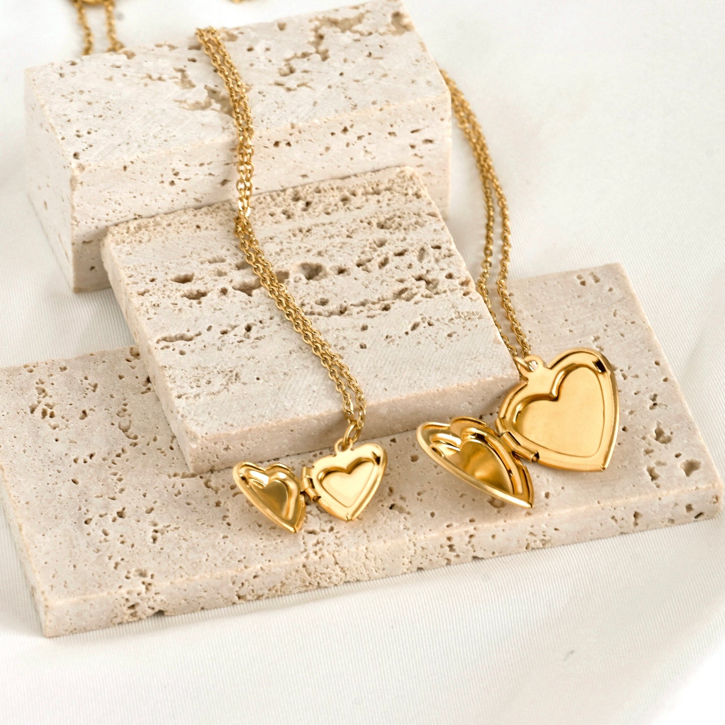 Gold heart-shaped open lockets on a textured stone surface