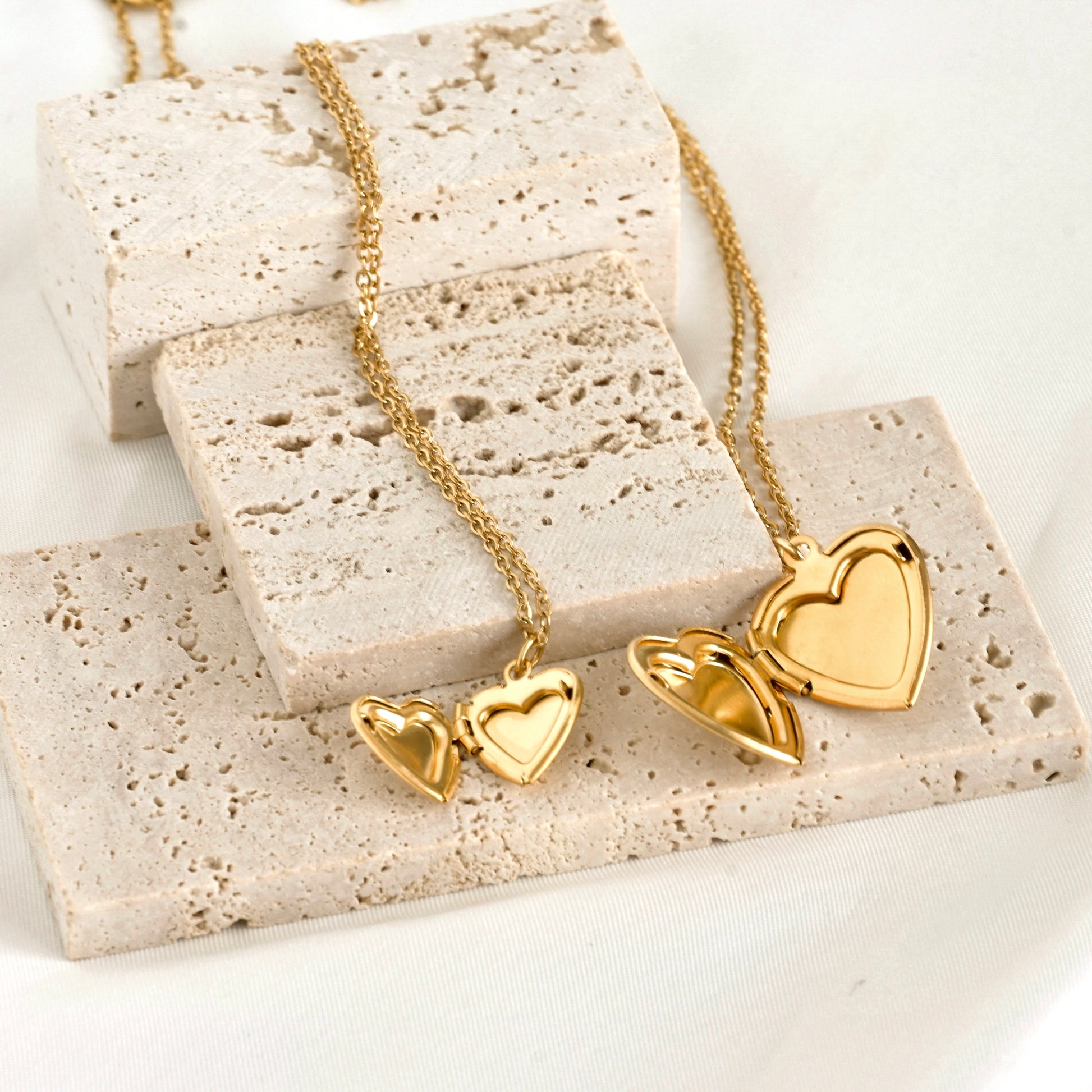 Gold heart-shaped open lockets on a textured stone surface
