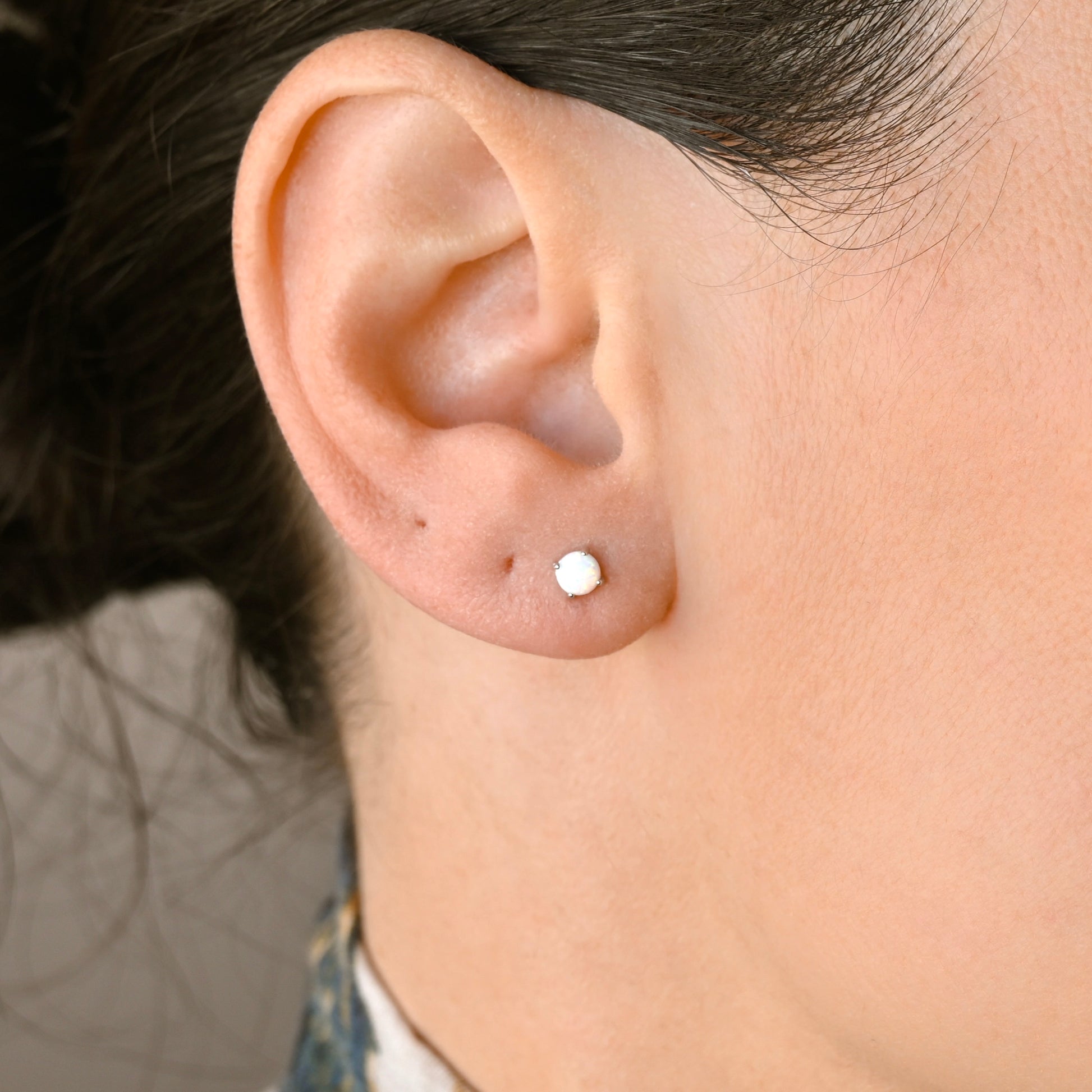 A close-up of a person's ear wearing a small, round, silver stud earring with opal center.