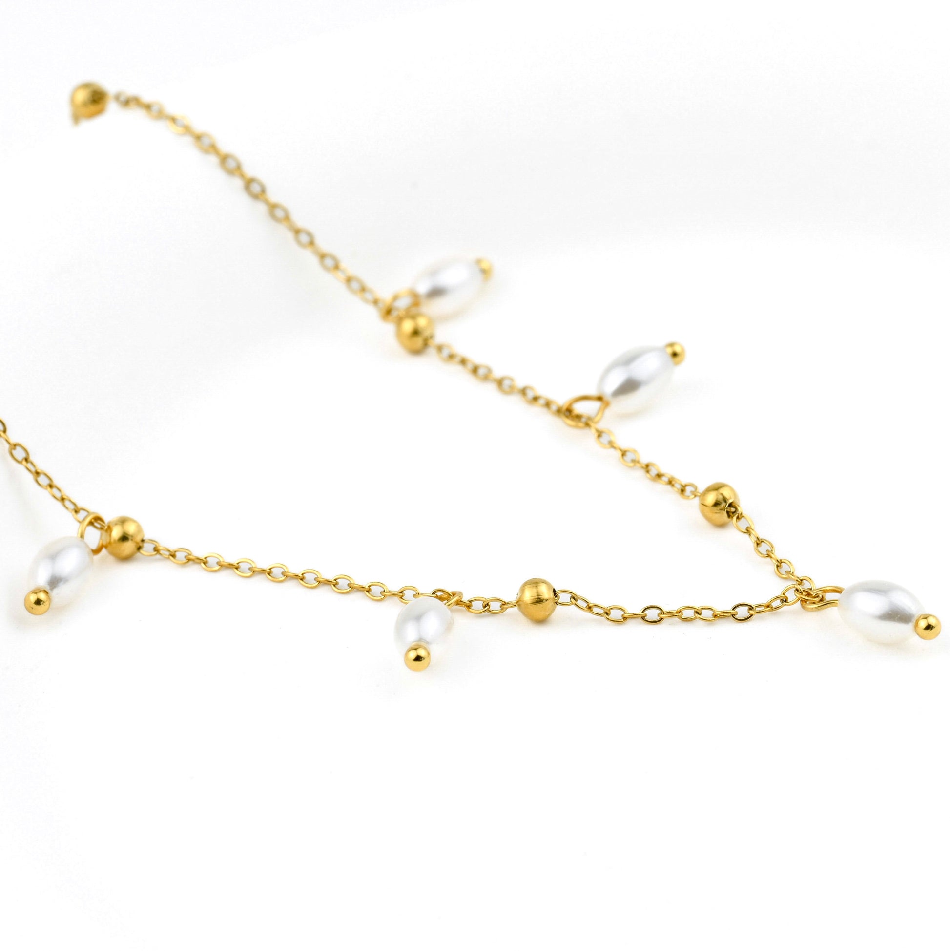 Gold necklace with teardrop shaped pearl drops along a beaded cable chain on a white background