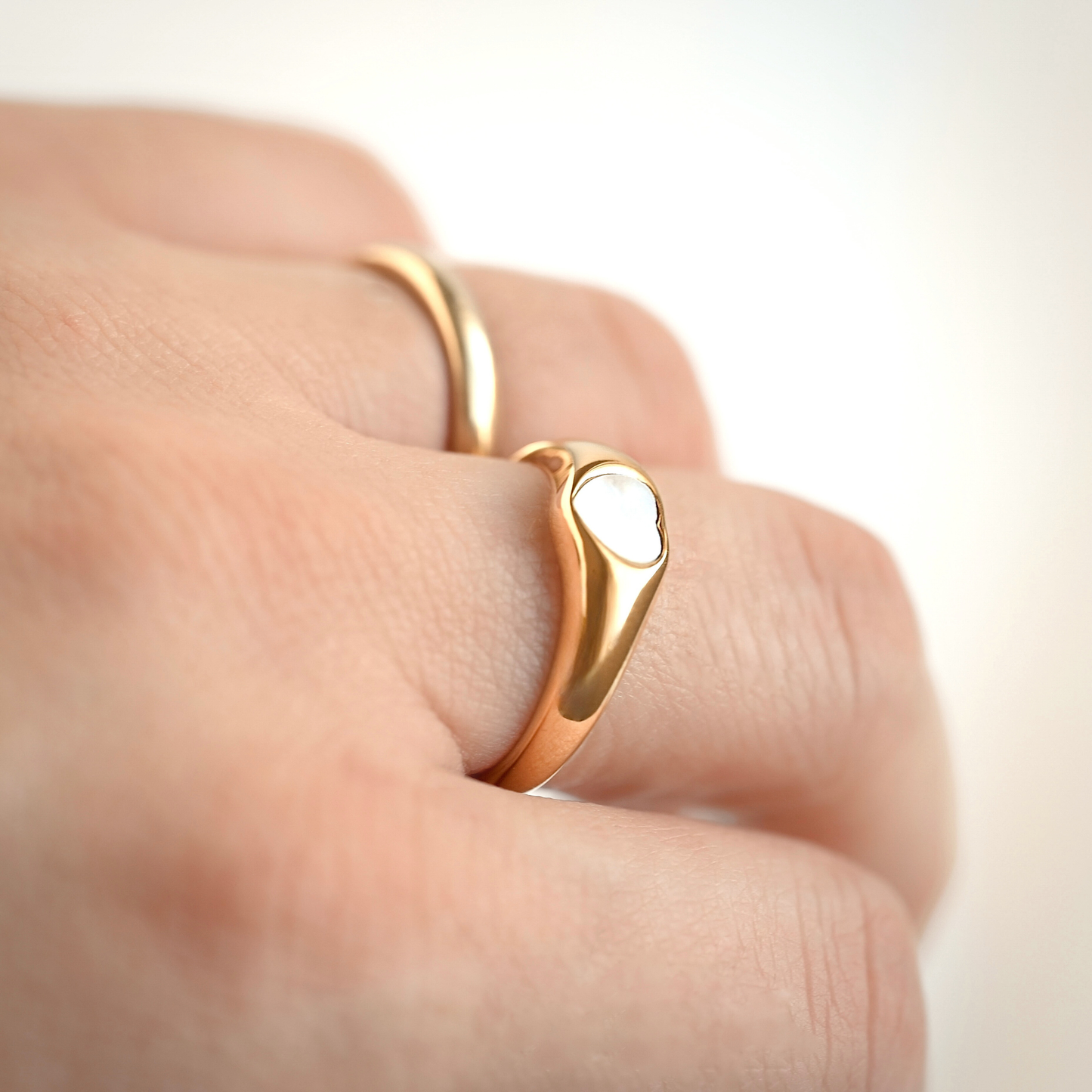 Gold mother of pearl  ring on a finger against a light background