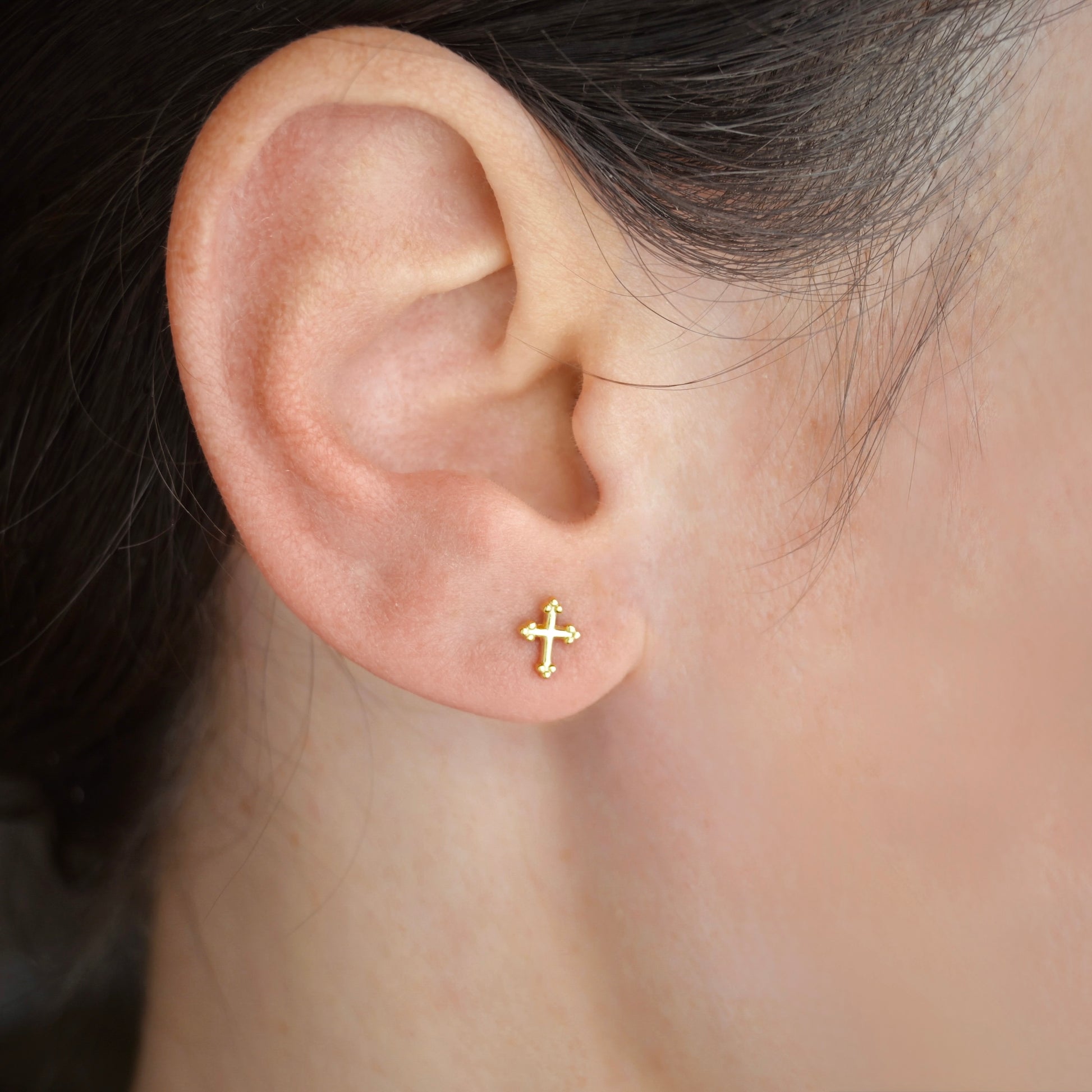 Gold cross earring on a person's ear with a blurred background