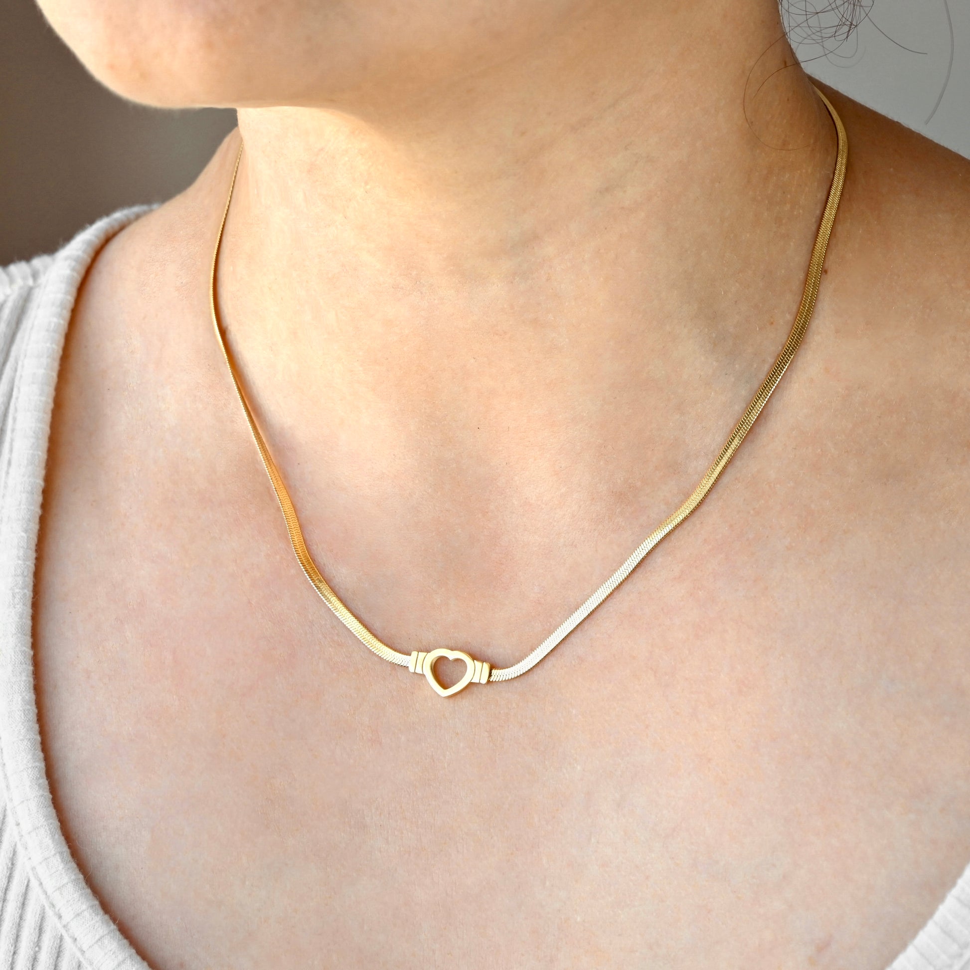 Gold herringbone necklace with a heart pendant worn by a person