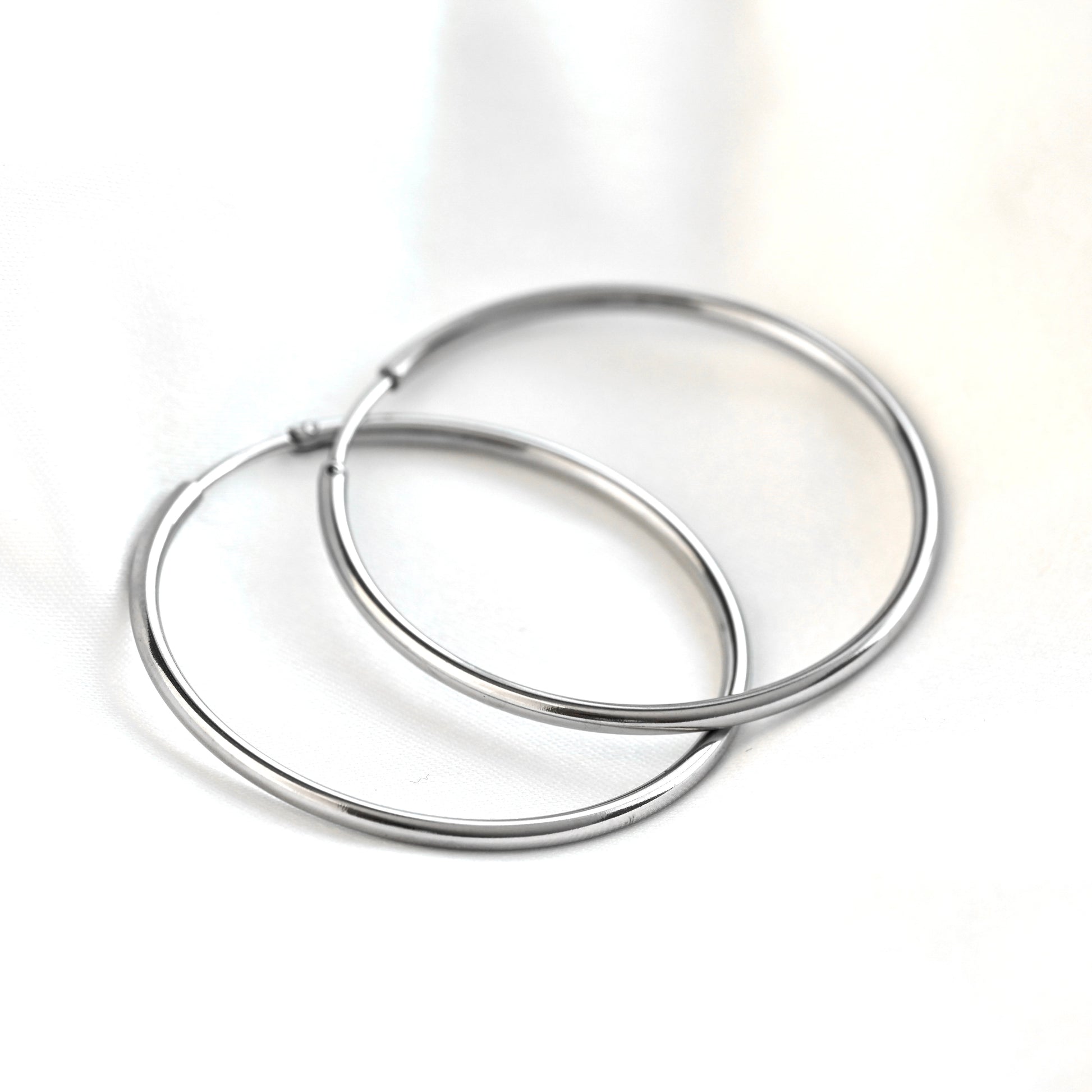 A pair of polished silver-tone hoop earrings overlapping on a clean white background.