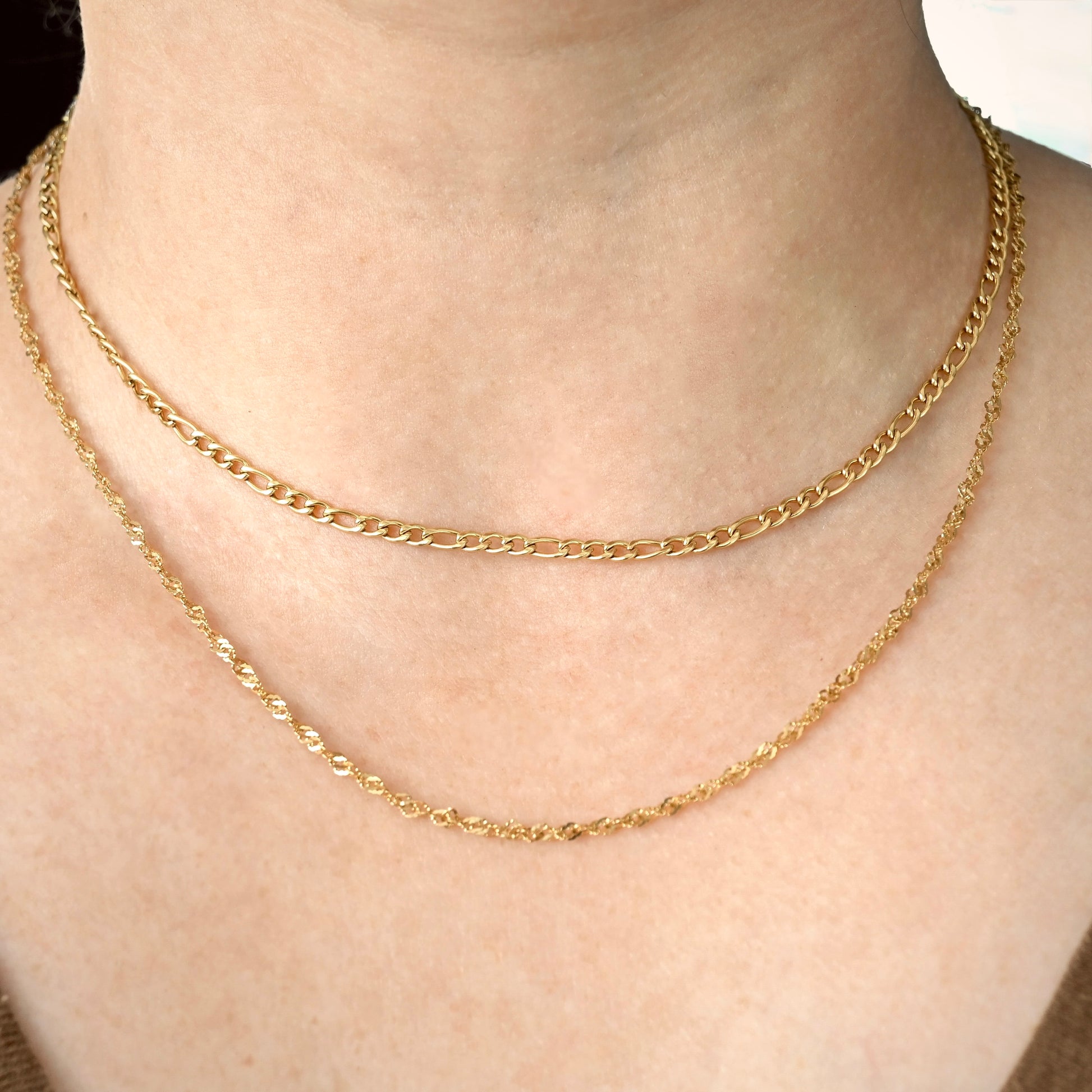 Gold twisted chain layered with a shorter figaro necklace on a person's neck