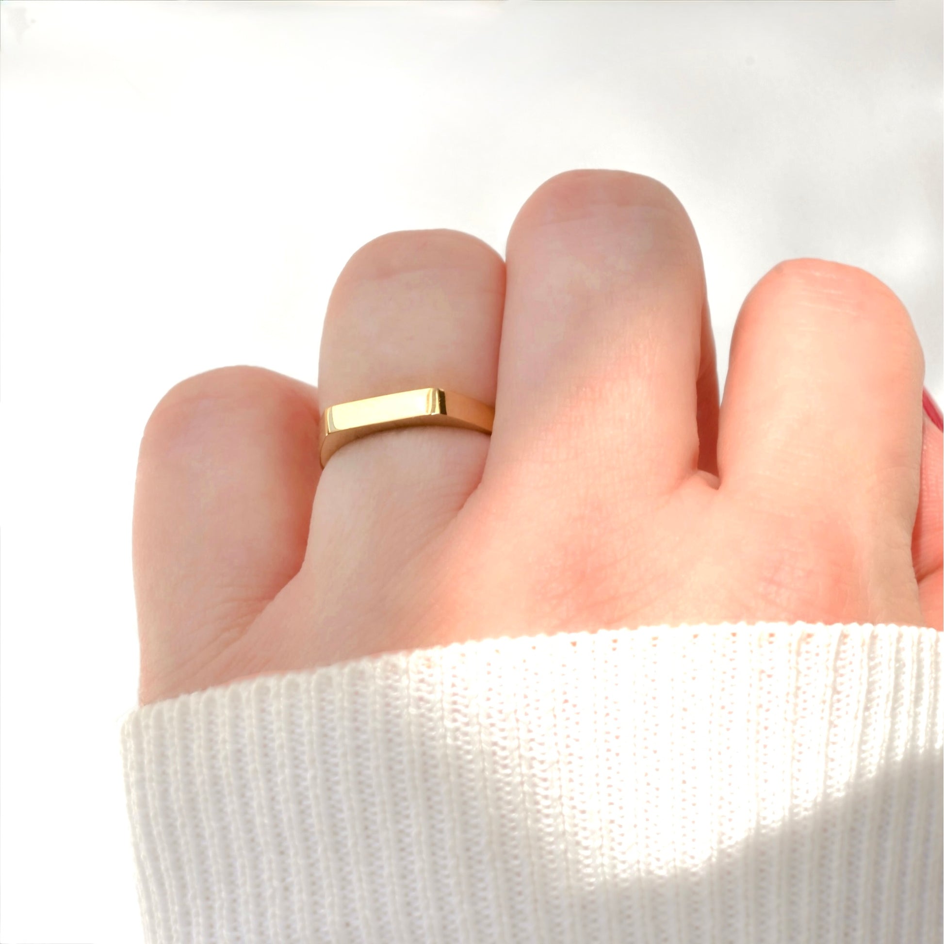 Gold bar ring with no engraving on a person's finger with a white sleeve background