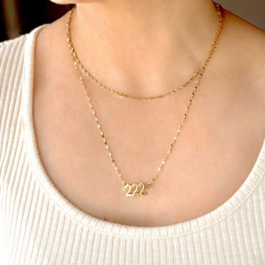 Gold mariner chain necklace with a '222' pendant on a person wearing a white top.