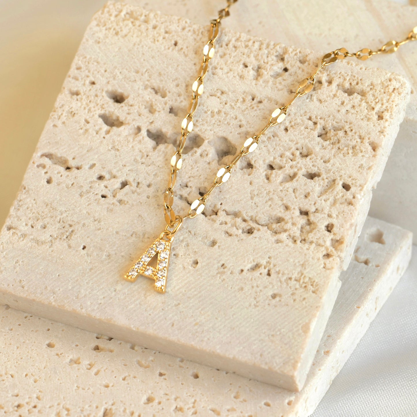 Gold necklace with a cz letter 'A' pendant on a textured stone surface