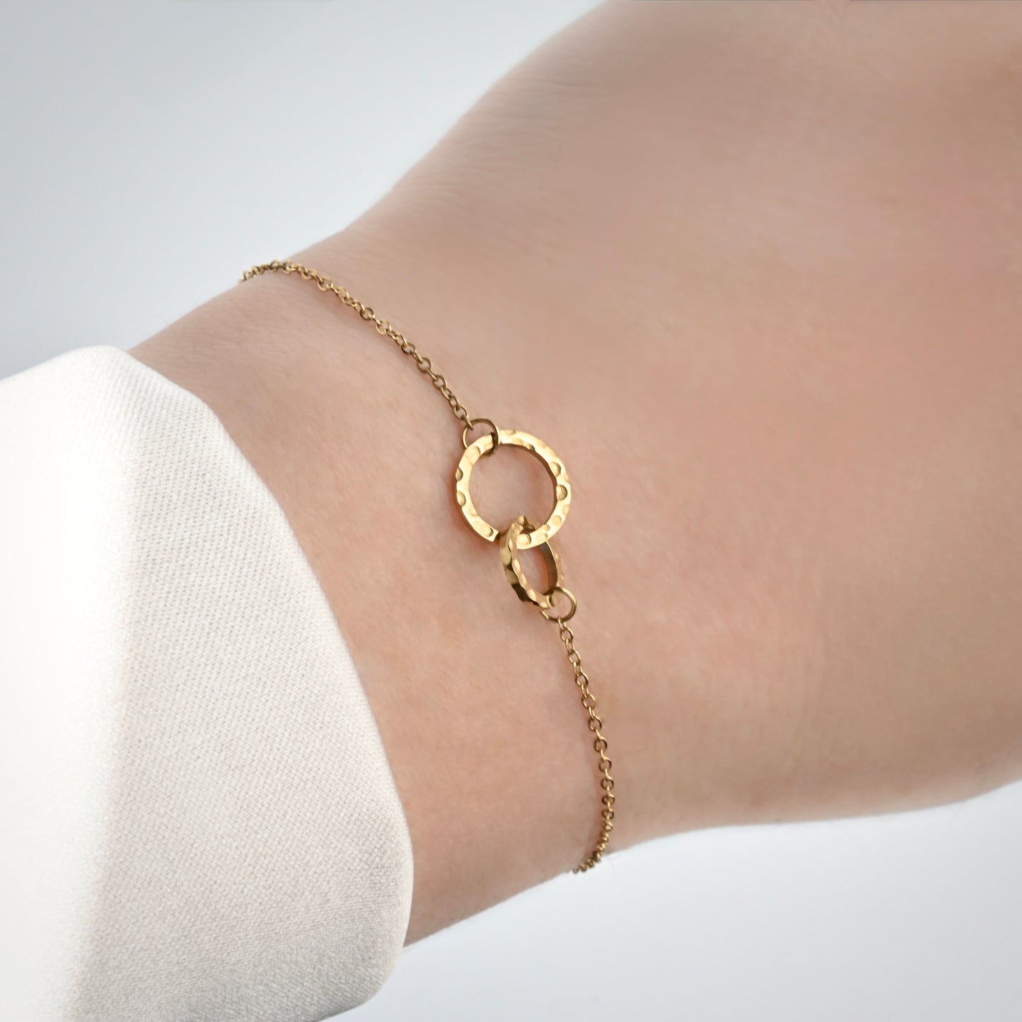 Gold hammered interlocking circles bracelet on a wrist with a plain background