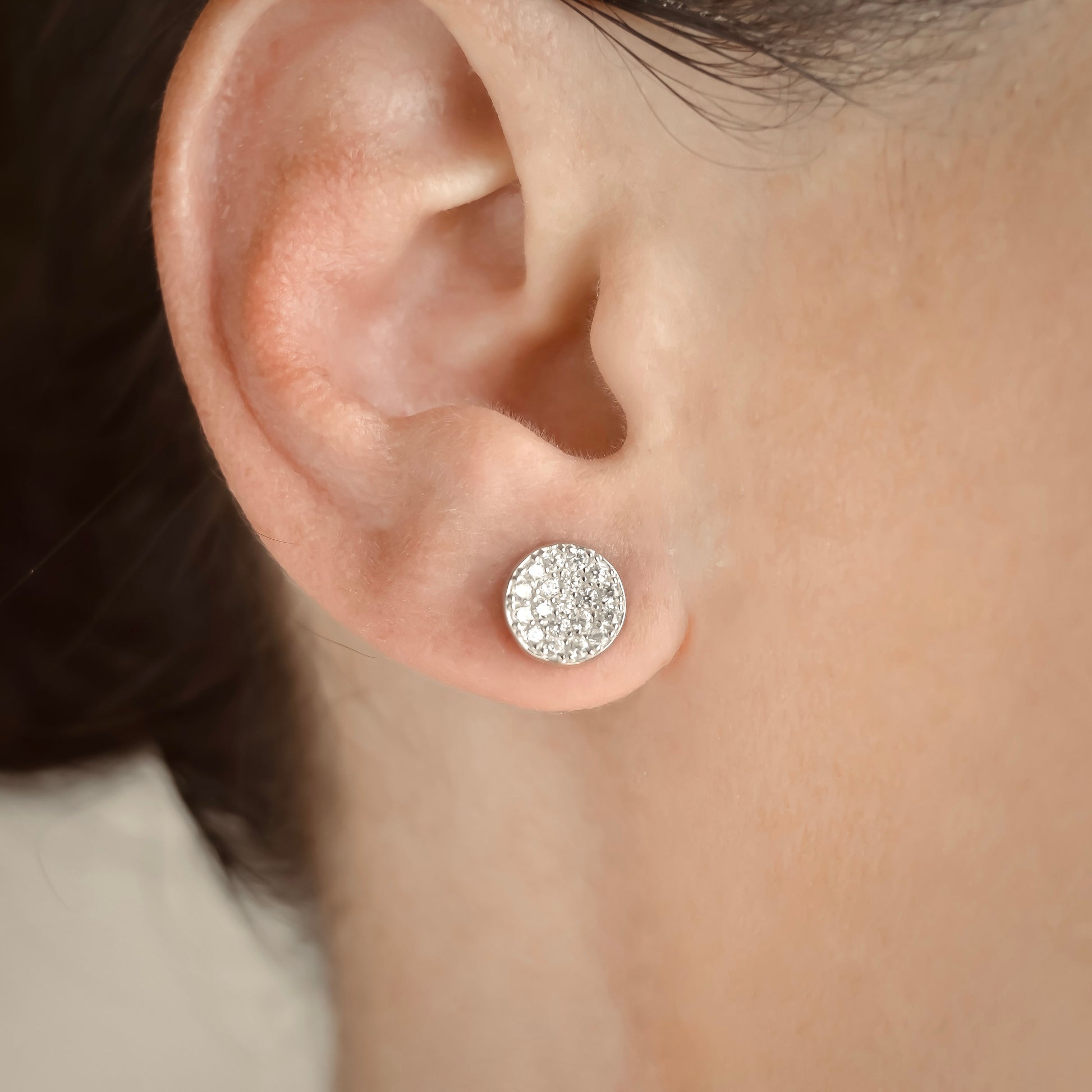 Close-up of an ear wearing a sparkling silver disc earring.