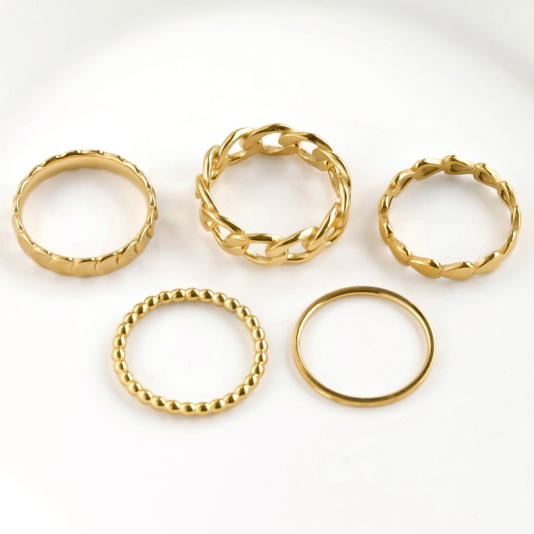 Top view of five gold rings with different designs on a white background