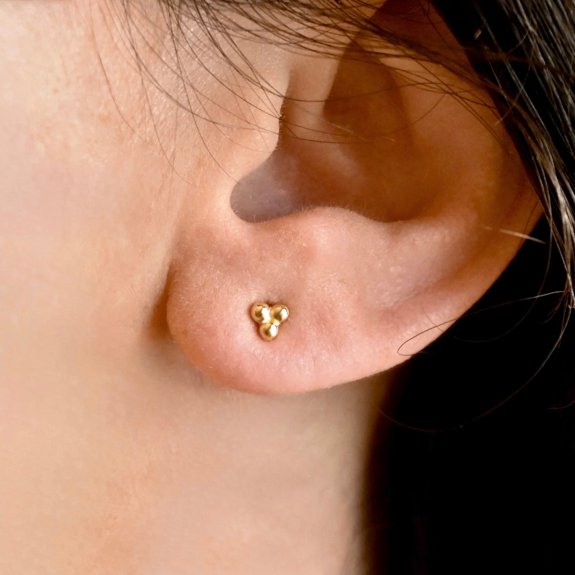 A close-up of a person's ear wearing a small gold stud earring with three clustered balls.