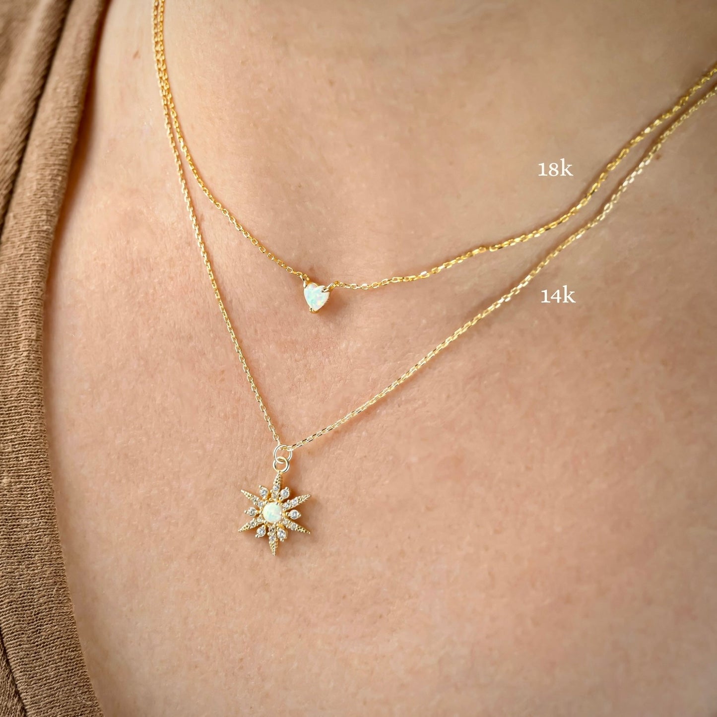 Two gold necklaces with heart and north star pendants on a person's neck, one labeled '18k' and the other '14k'.
