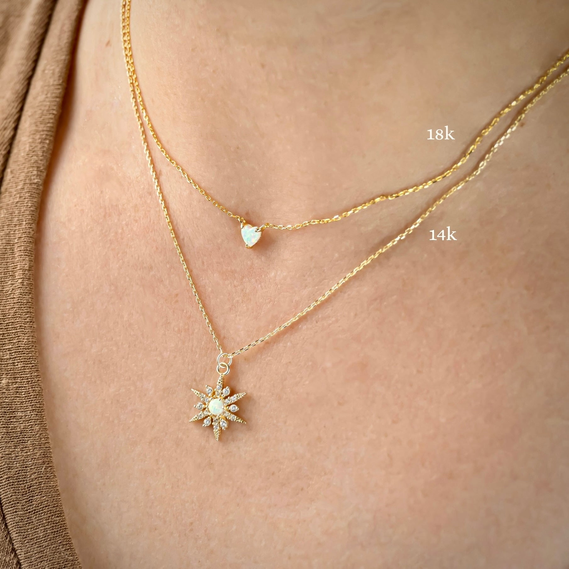 Two gold necklaces with heart and north star pendants on a person's neck, one labeled '18k' and the other '14k'.