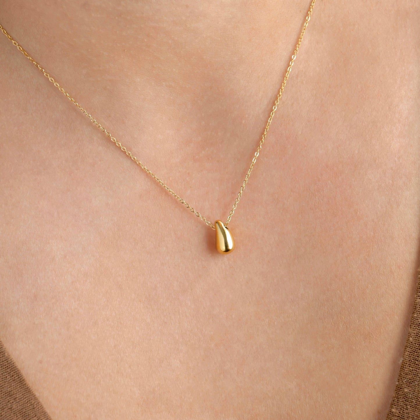 Gold necklace with a small gold teardrop pendant on a person's neck