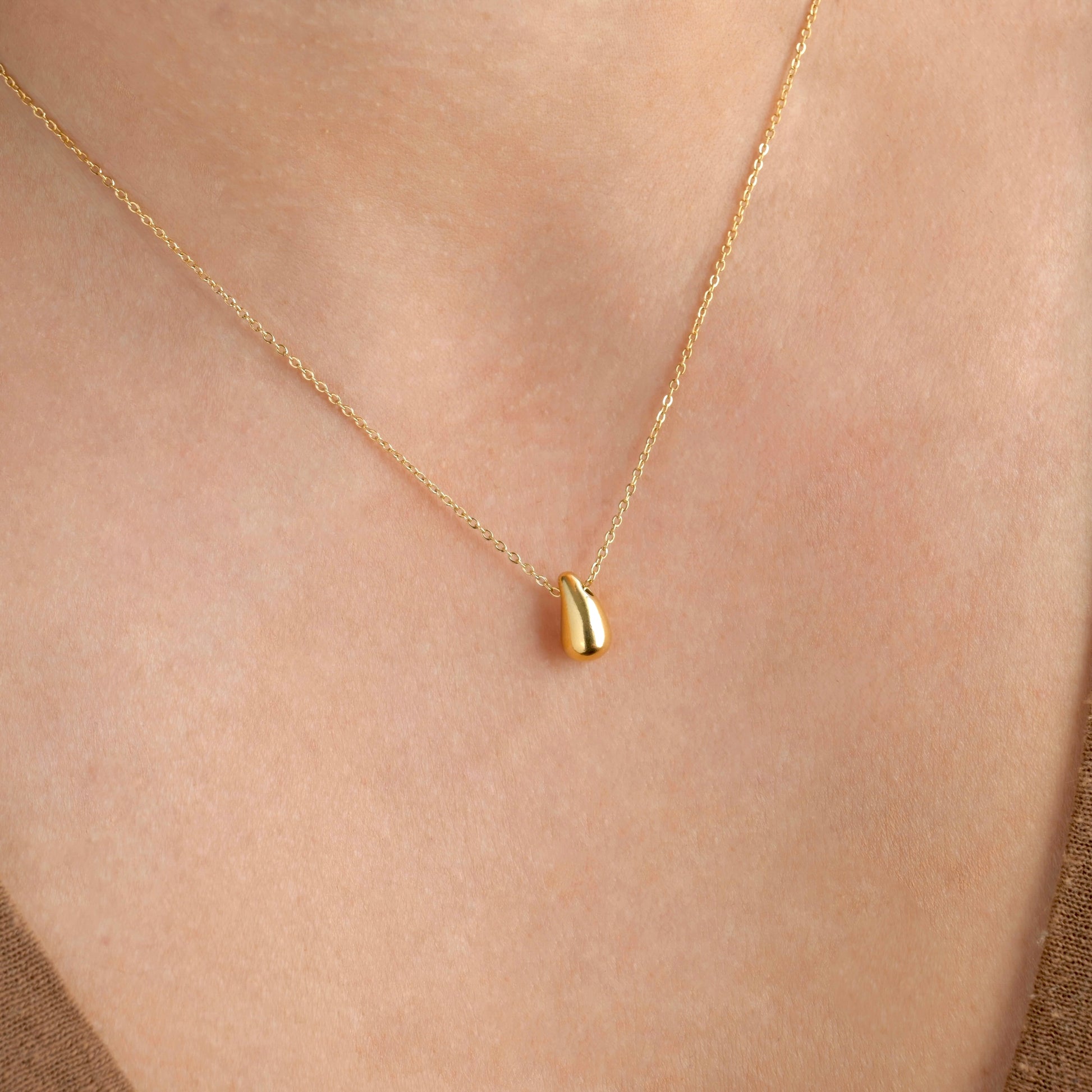Gold necklace with a small gold teardrop pendant on a person's neck