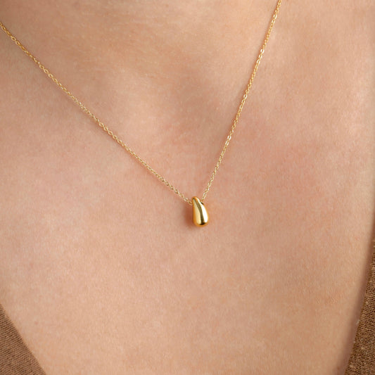 Gold necklace with a small gold teardrop pendant on a person's neck