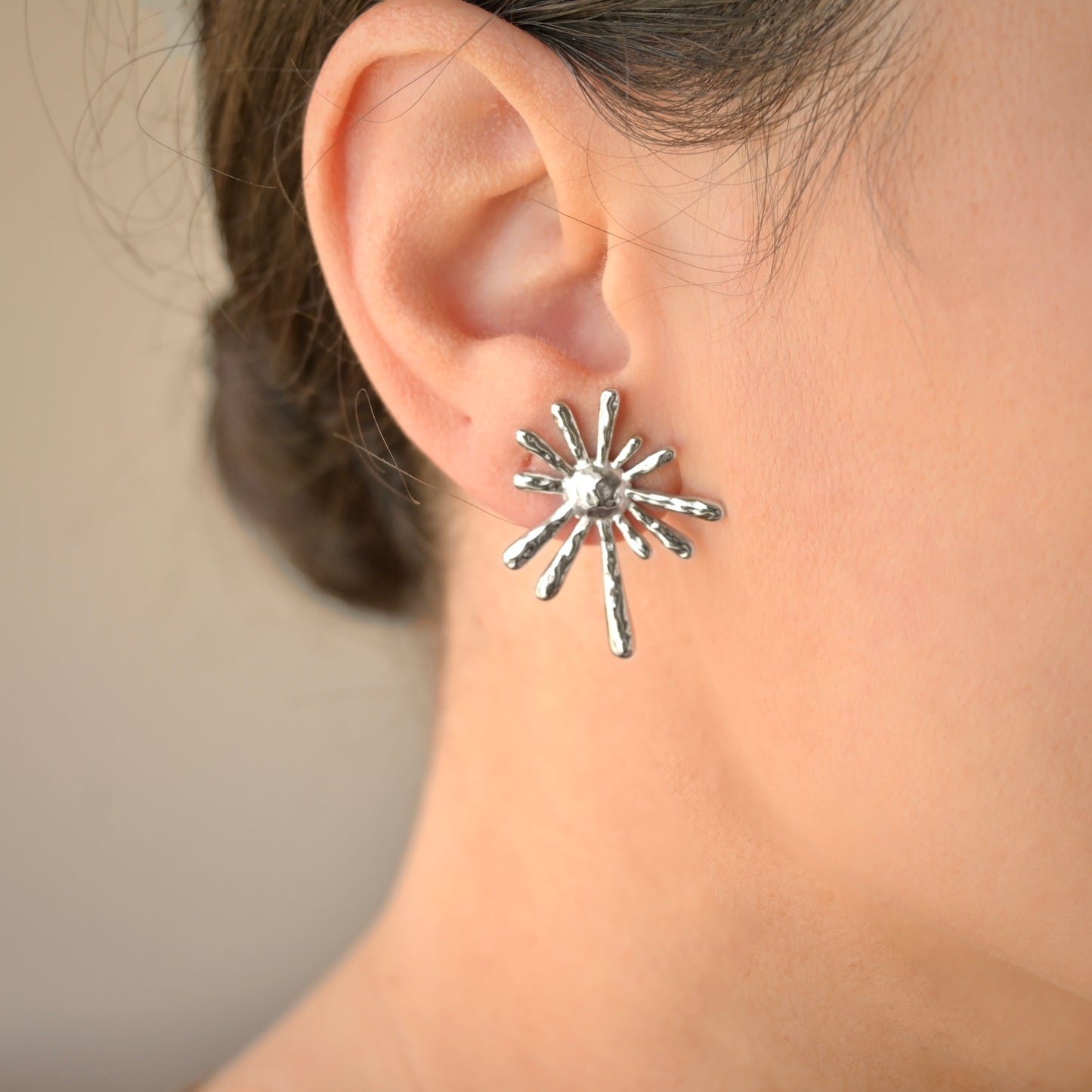 Silver star-shaped earring worn by a person with a neutral background