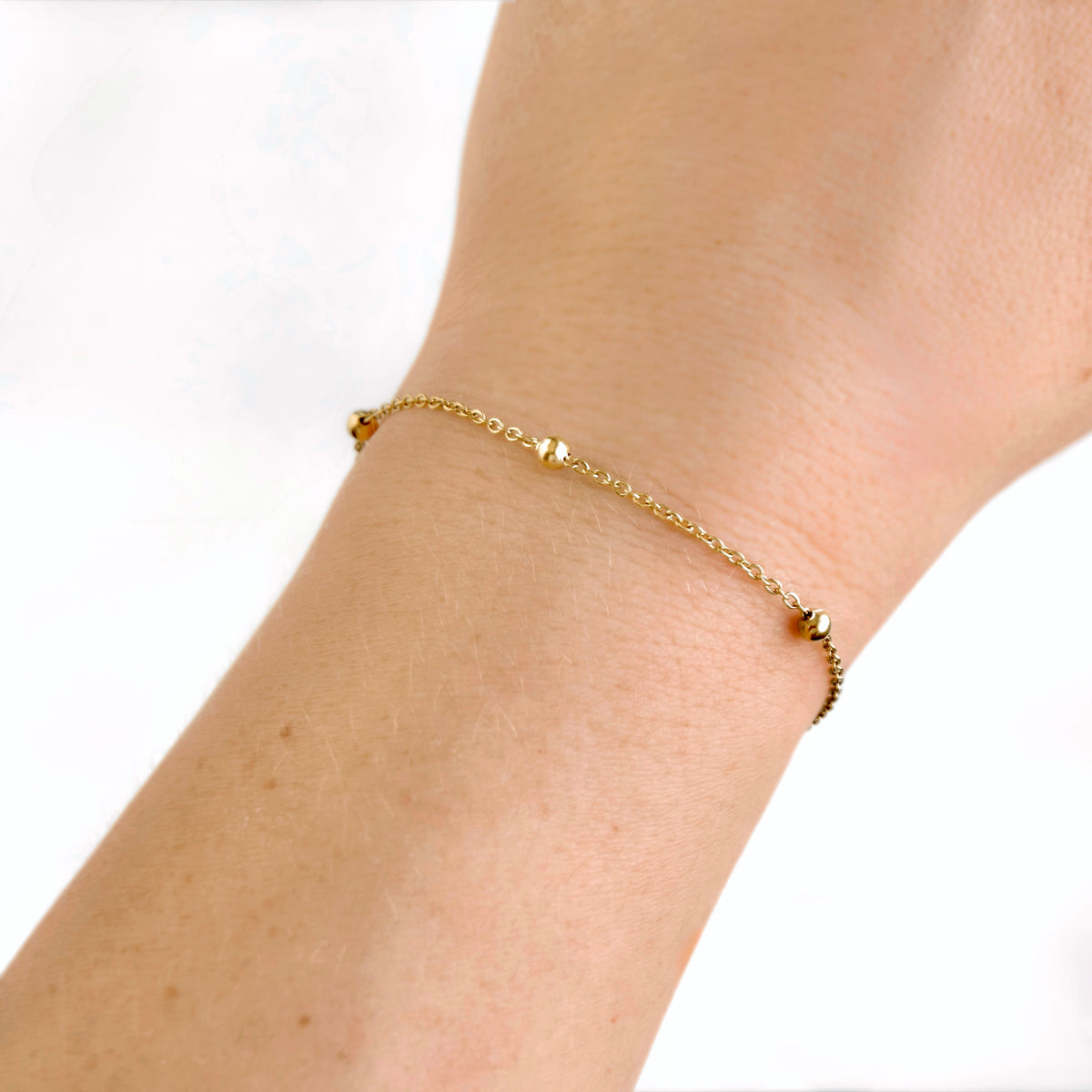 A delicate gold chain bracelet with small bead accents, shown worn on a person's wrist against a plain white background.