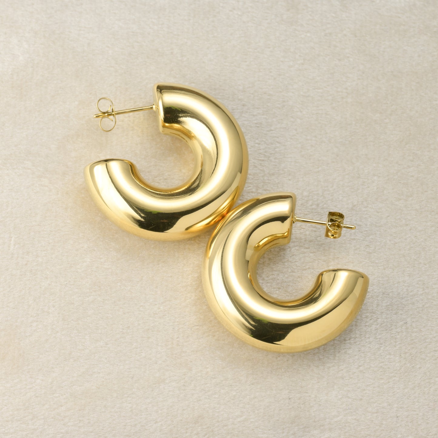 Thick Gold hoop earrings on a light beige background