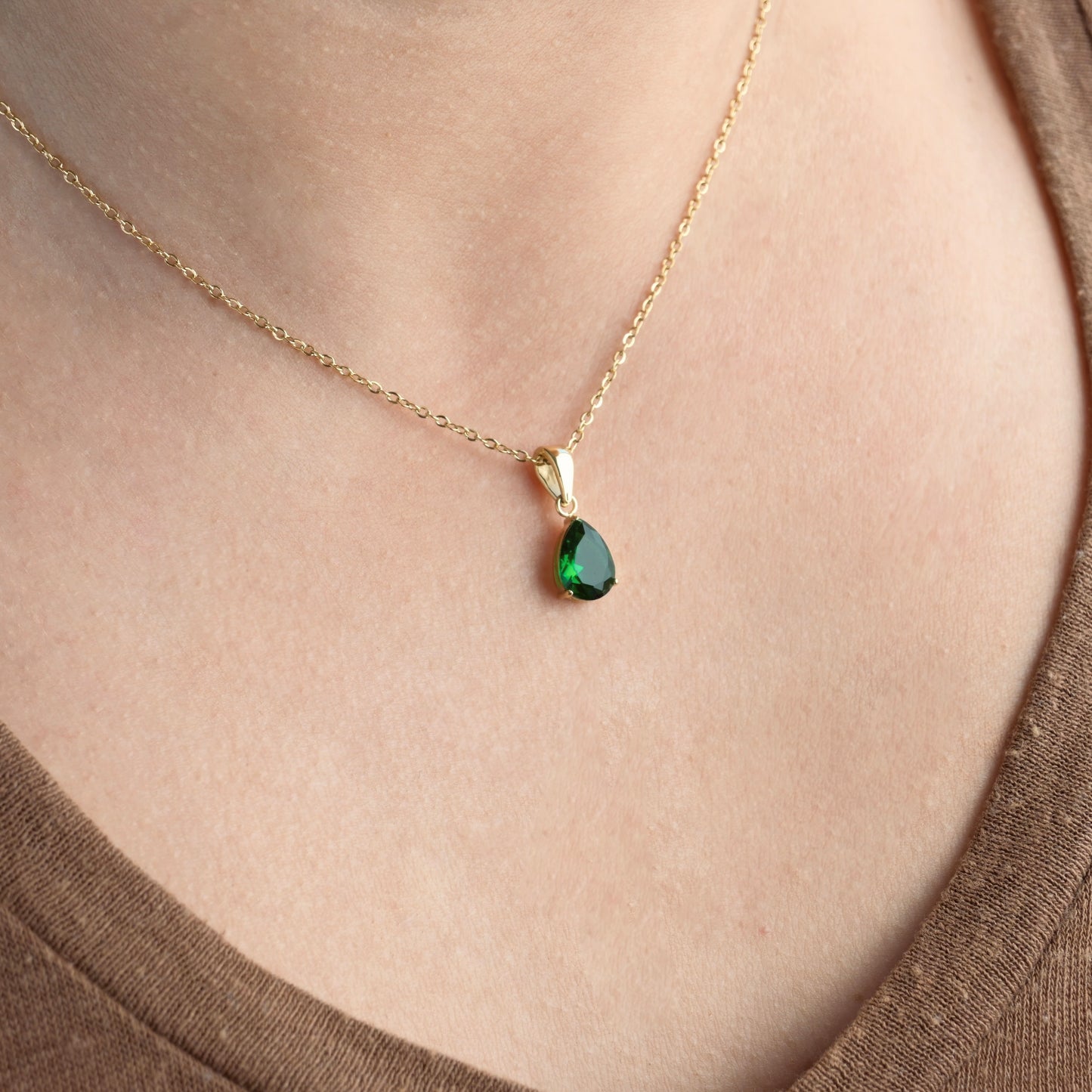 Gold may birthstone pendant on a person's neck.